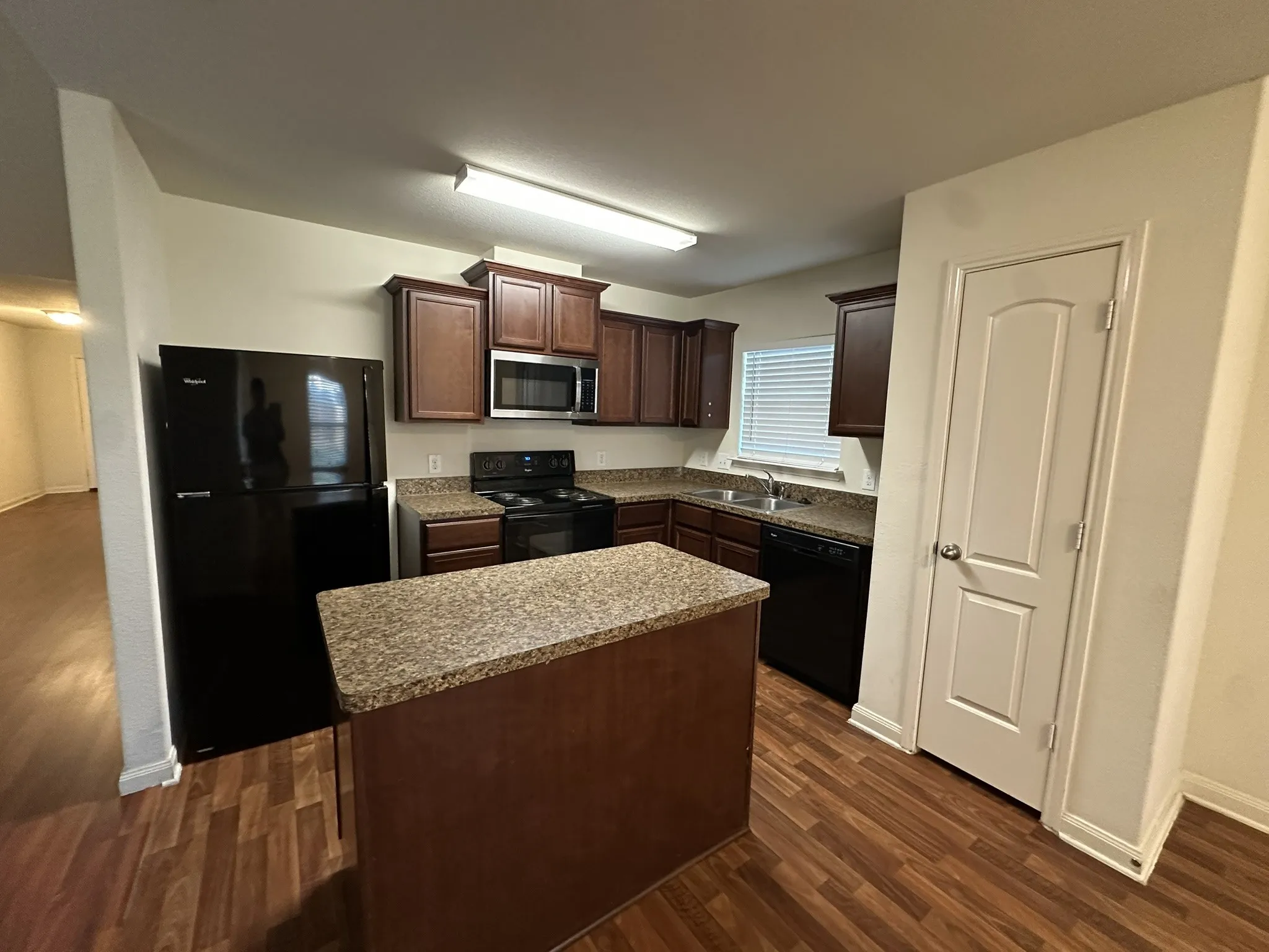Kitchen featuring wood-finish flooring, dark wood cabinetry, granite-style countertops, stainless steel microwave, and a central island