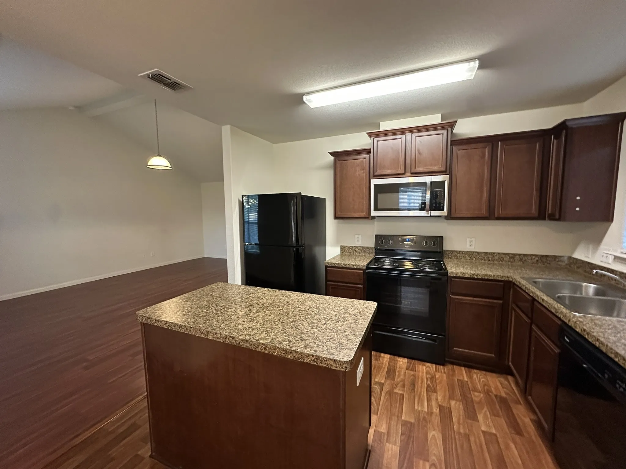 Kitchen featuring dark wood cabinetry, speckled countertops, and black appliances including a refrigerator, range, microwave, and dishwasher