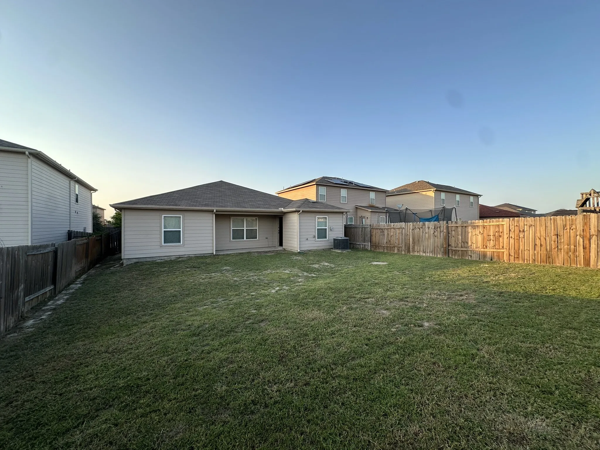 Spacious backyard featuring a manicured lawn, a full wood privacy fence, and a neutral-toned exterior with multiple windows