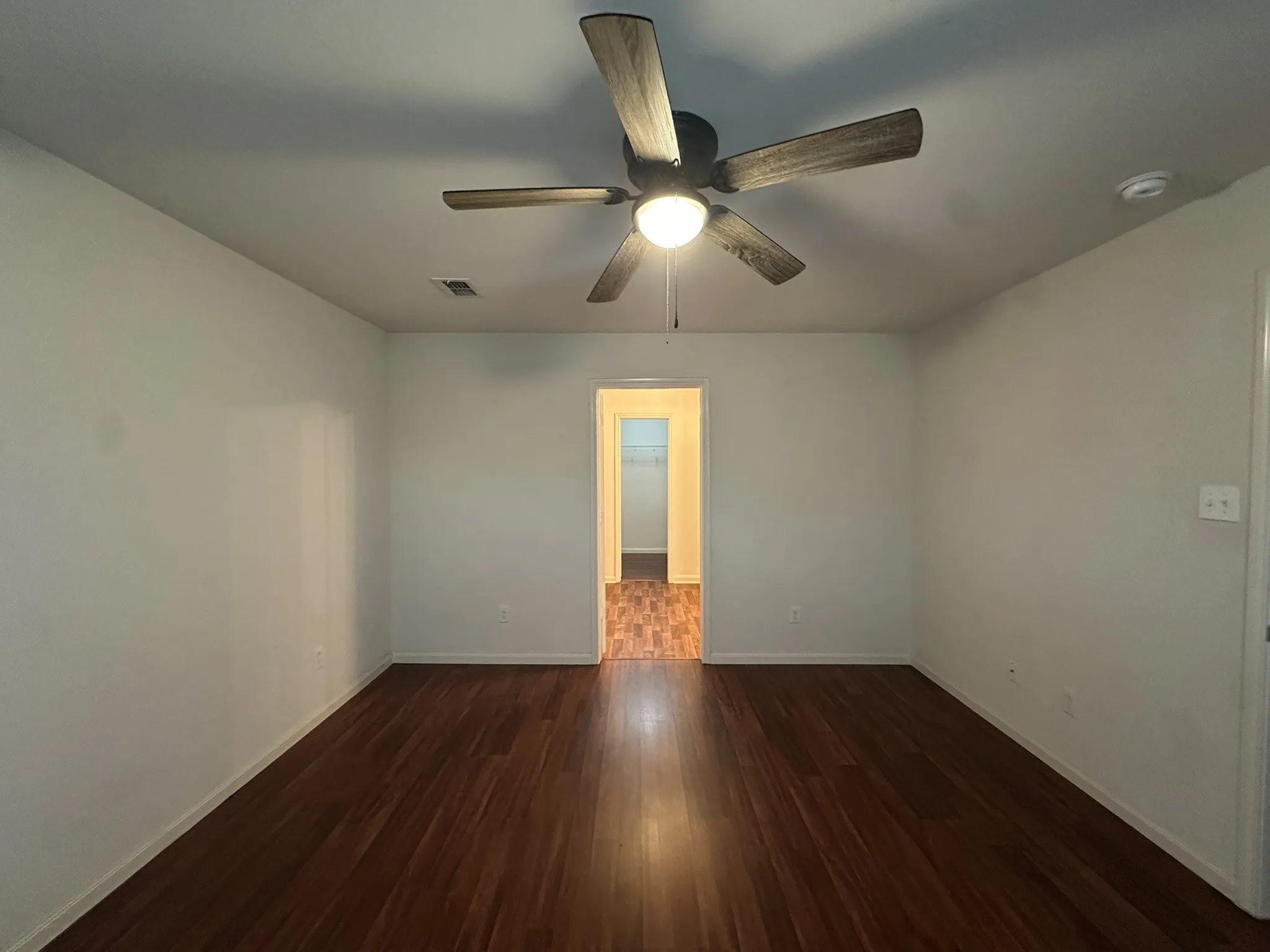 Spacious room featuring rich wood-finish flooring, a ceiling fan with integrated lighting, and neutral wall tones
