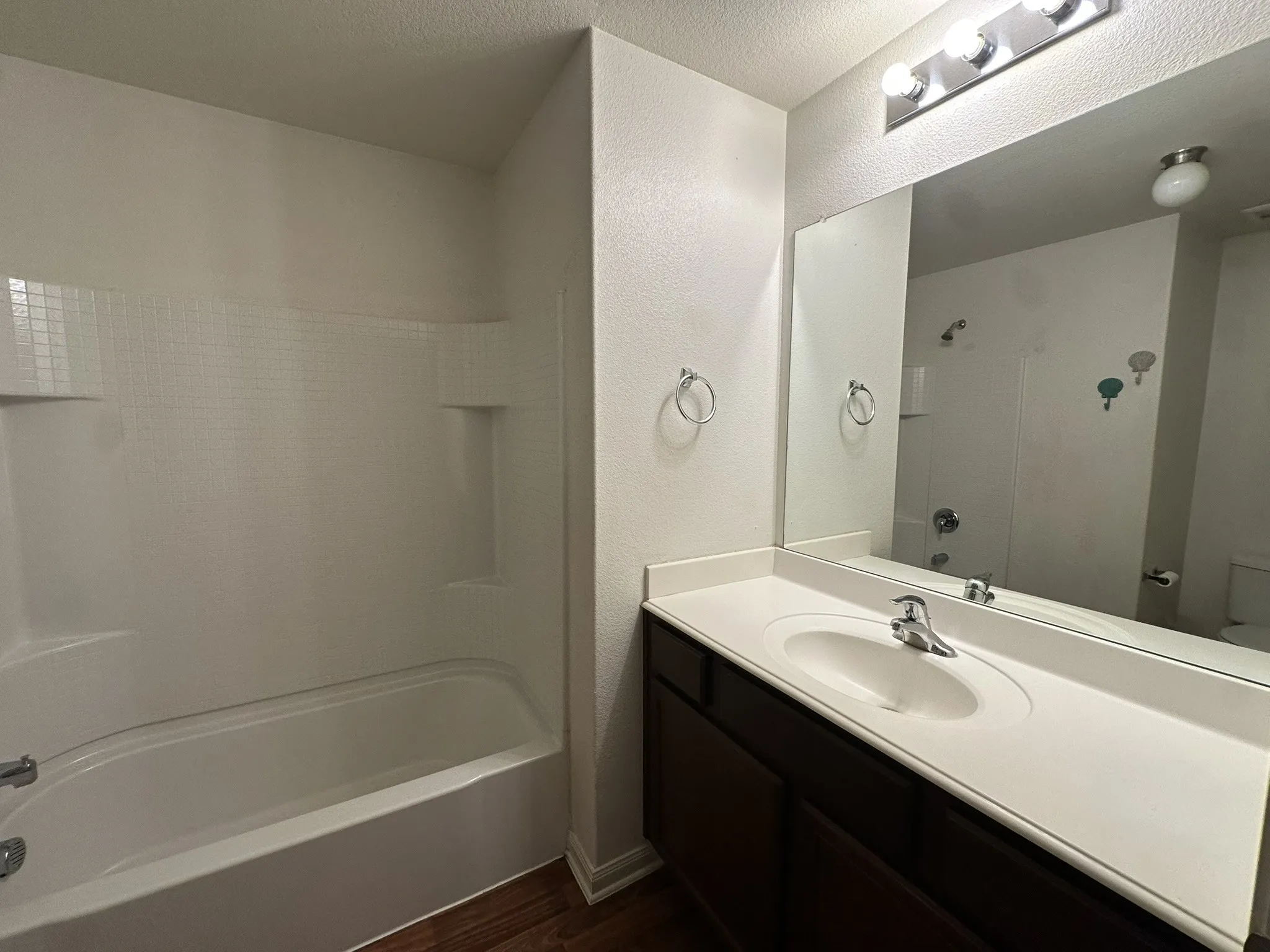 Bathroom featuring a combined shower and tub with built-in shelving, dark wood-finish vanity with an integrated sink and white countertop, and a wall-mounted mirror with overhead bar lighting