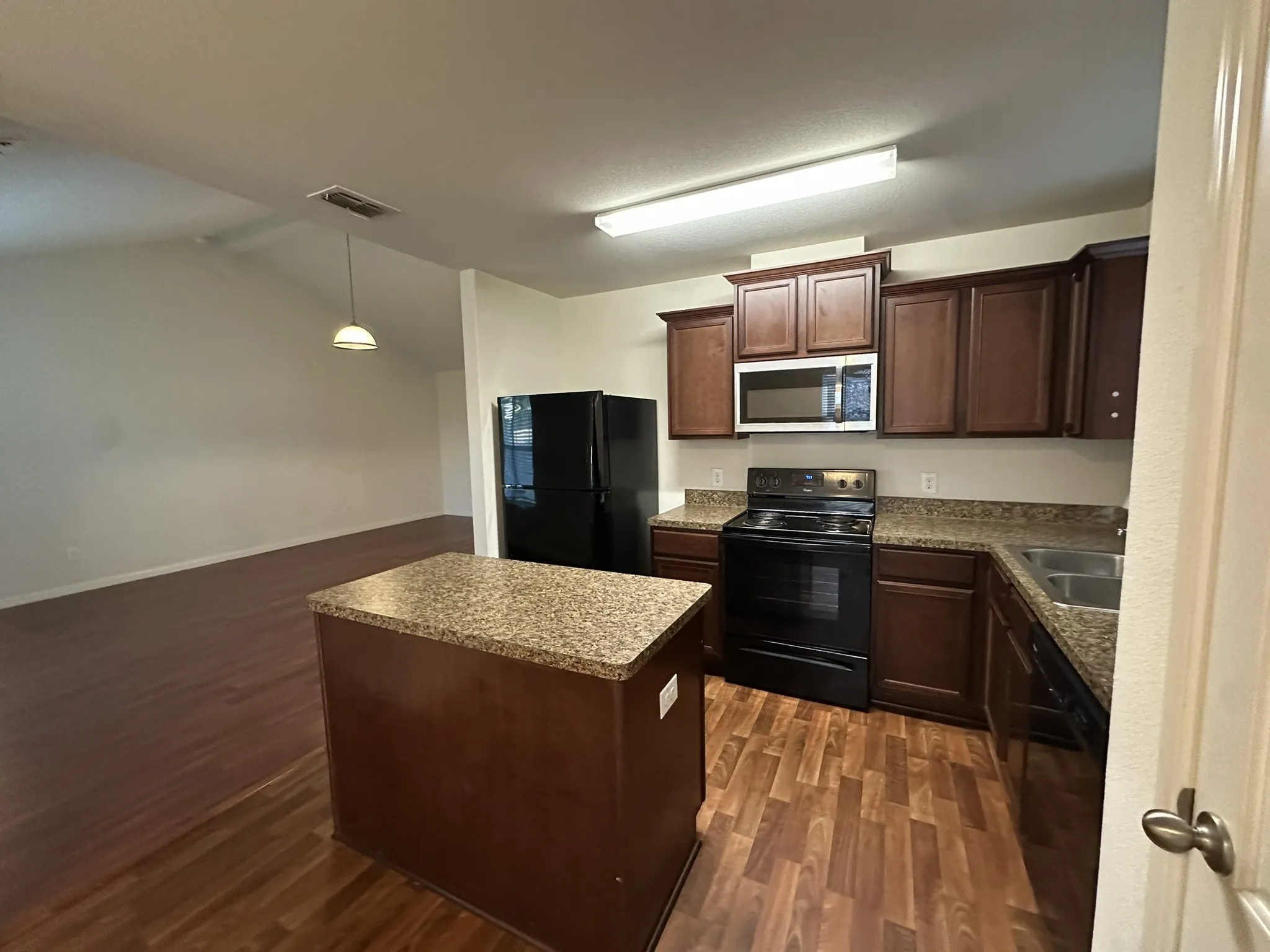 Kitchen featuring dark wood cabinetry, granite-style countertops, and black appliances including a microwave, range, and refrigerator