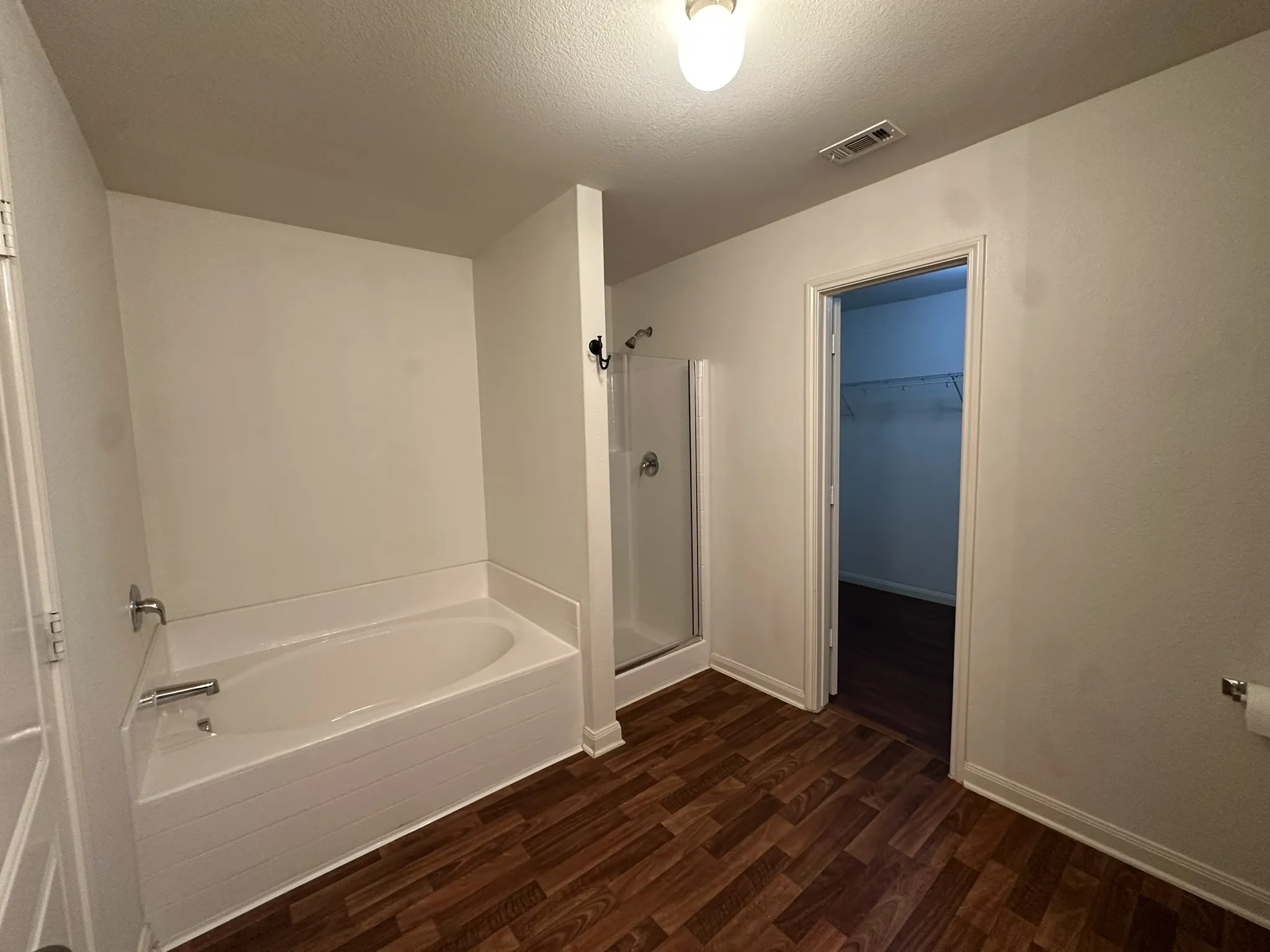 Bathroom featuring a built-in soaking tub, separate glass-enclosed shower, and wood-finish flooring