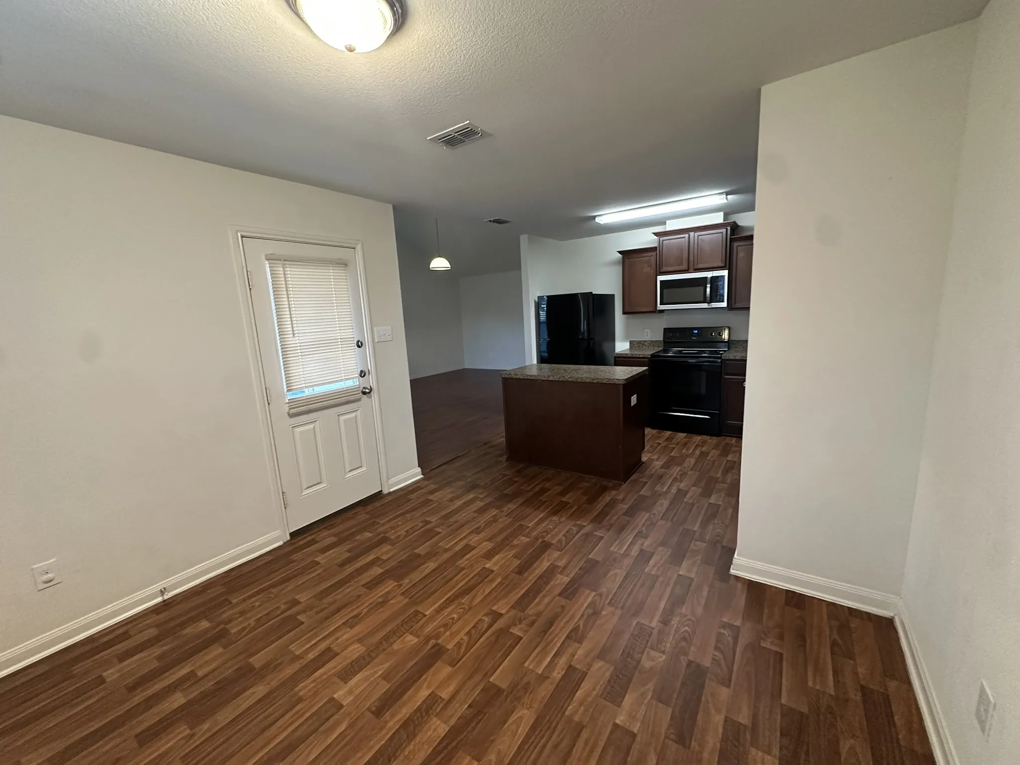 Open-concept kitchen and dining area featuring wood-finish flooring, dark wood cabinetry, and black appliances