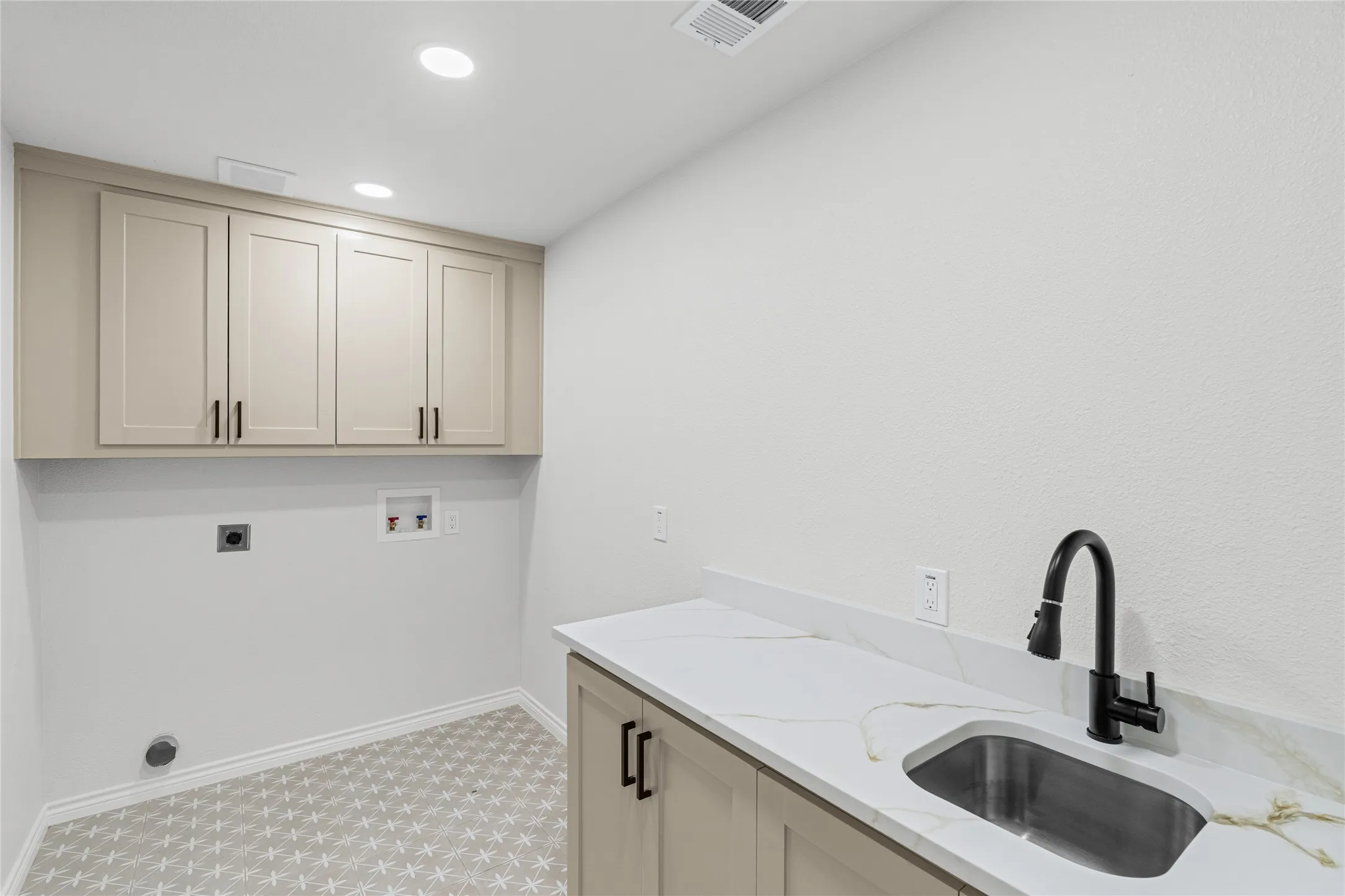 Functional utility space featuring light-colored cabinetry, white countertops, and a stainless steel sink with a matte black faucet