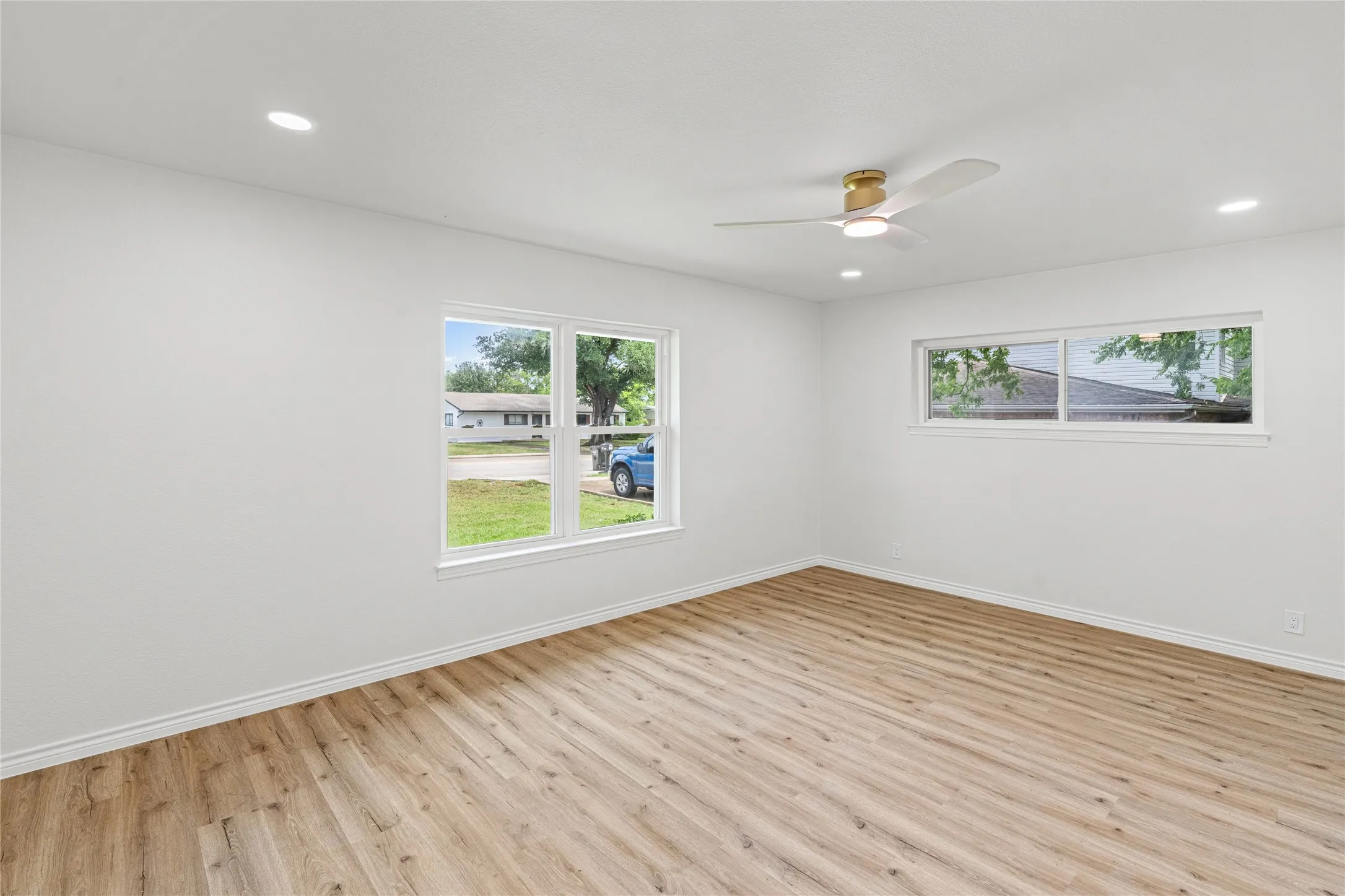 Spacious room featuring light wood-finish flooring, recessed lighting, and a modern ceiling fan with a gold-tone accent