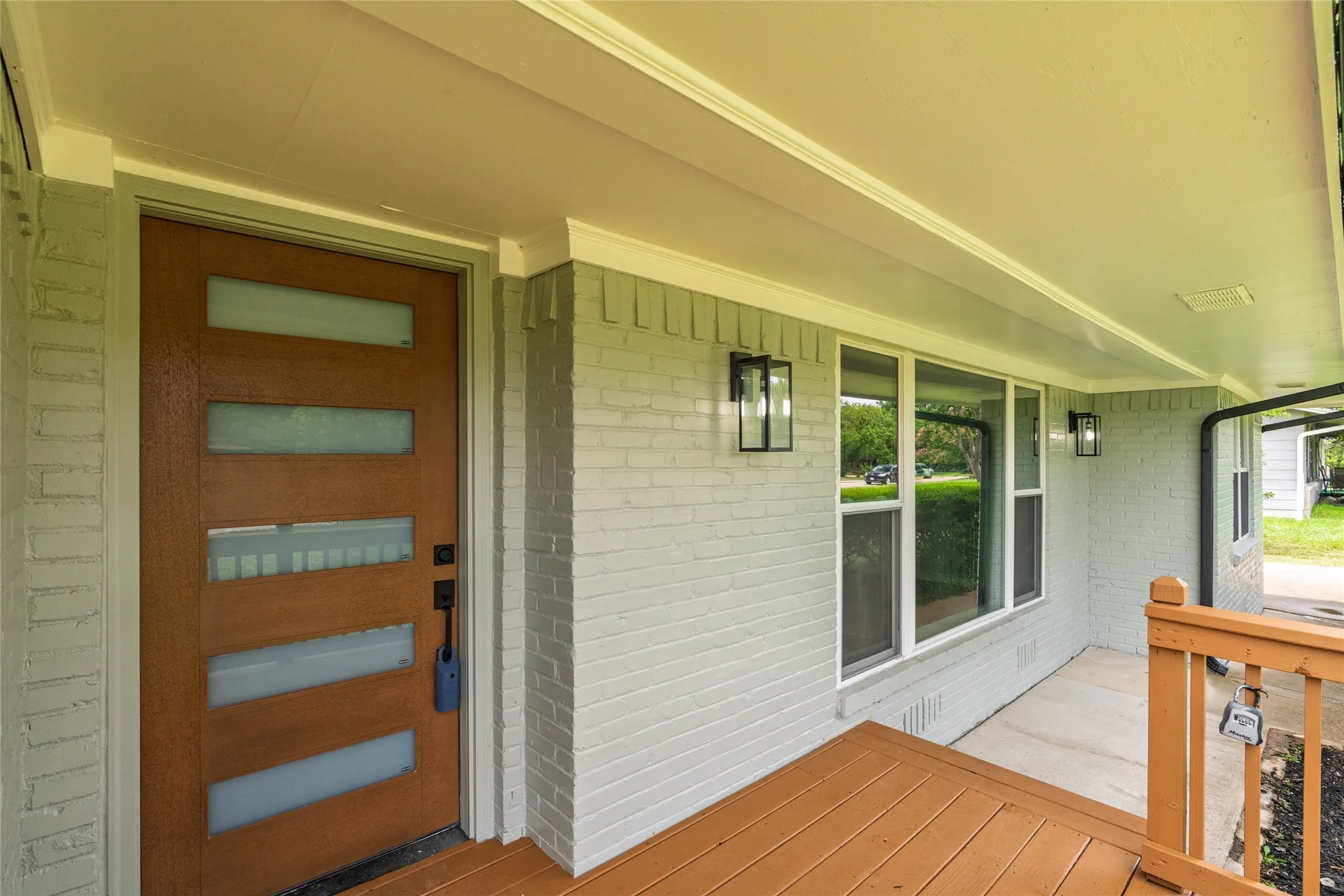 Front entry featuring a contemporary wood-finish door with frosted glass inserts, painted brick exterior, and a covered porch with wood-finish flooring