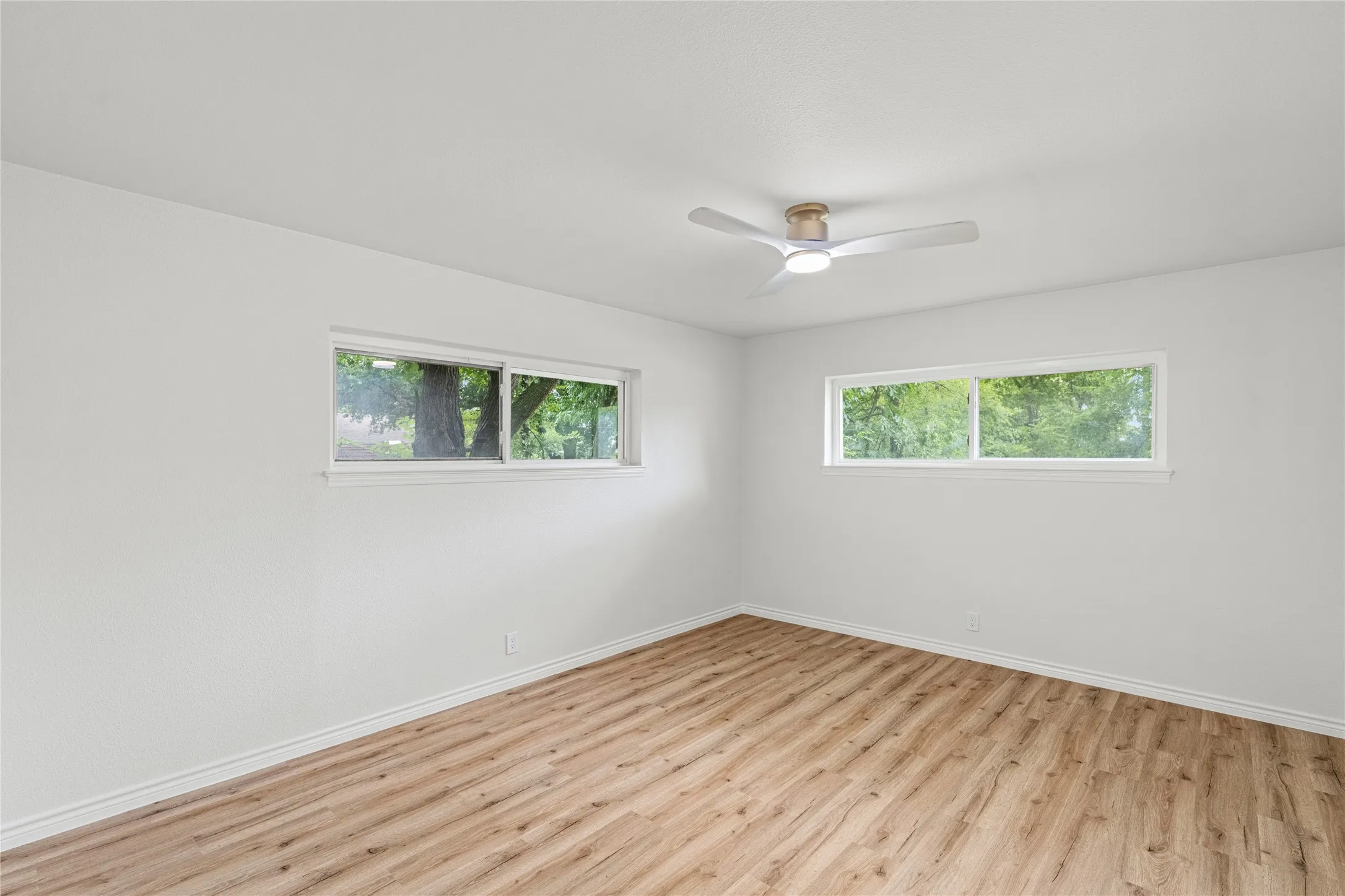 Spacious room featuring light wood-finish flooring, white walls, and two horizontal windows