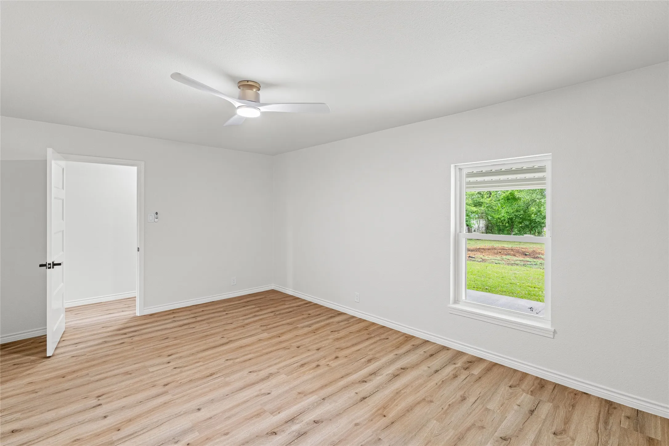 Spacious room featuring wood-finish flooring, crisp white walls, and a contemporary ceiling fan with integrated lighting