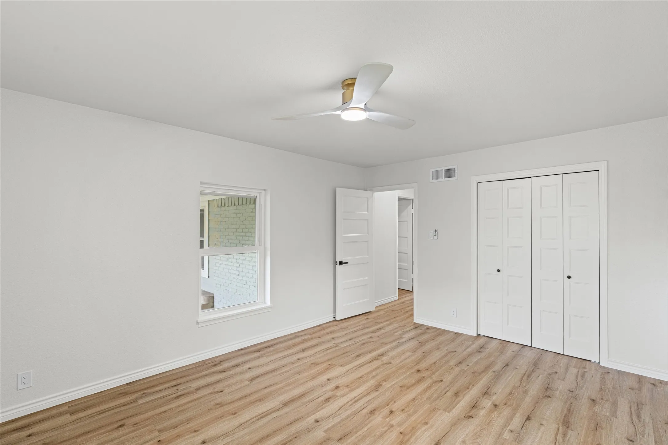 Spacious room featuring wood-finish flooring, white walls, and a contemporary ceiling fan