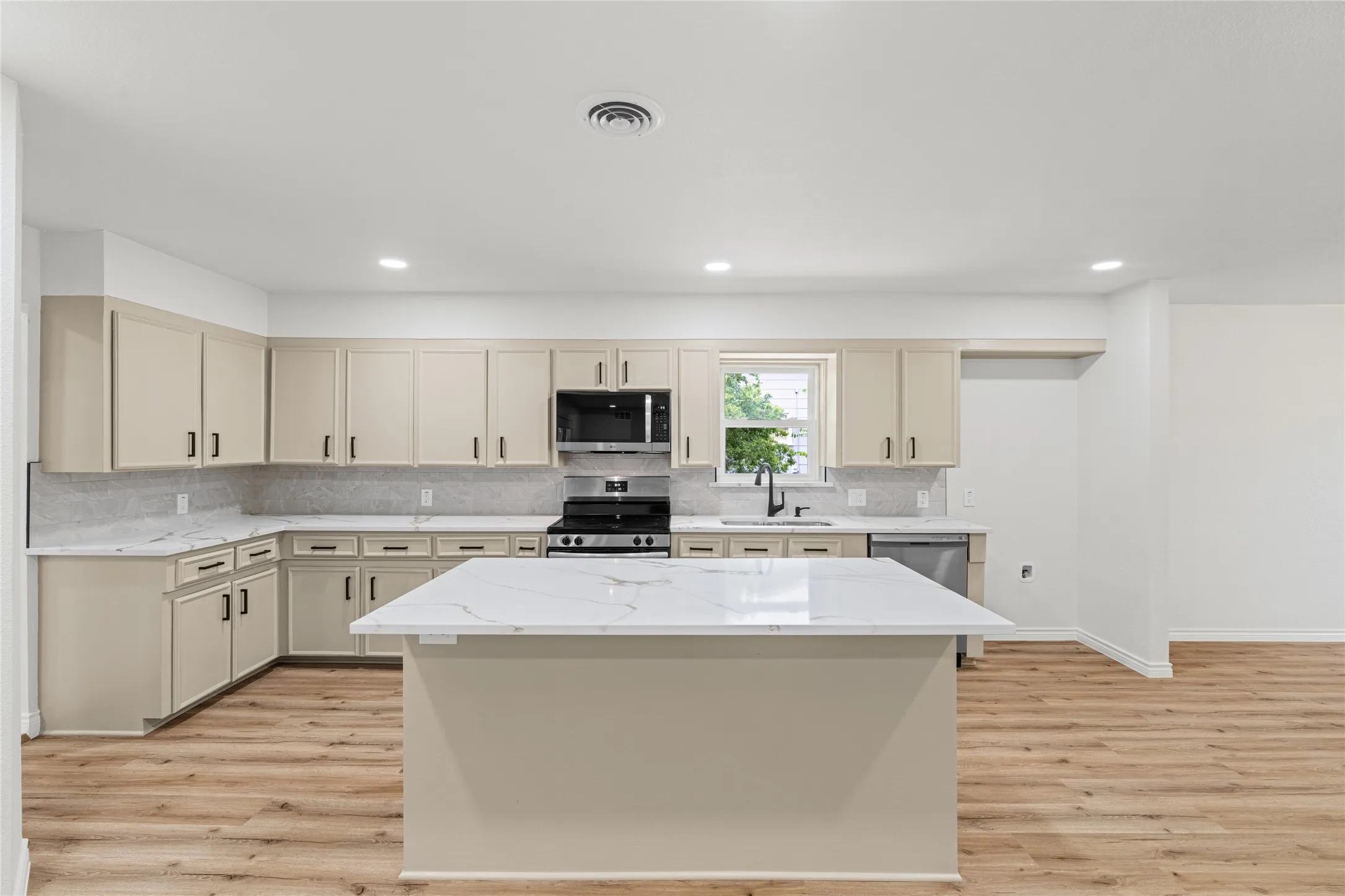 Well-appointed kitchen featuring an expansive central island with a solid surface countertop, wood-finish flooring, full suite of stainless steel appliances, and abundant cabinetry with modern hardware