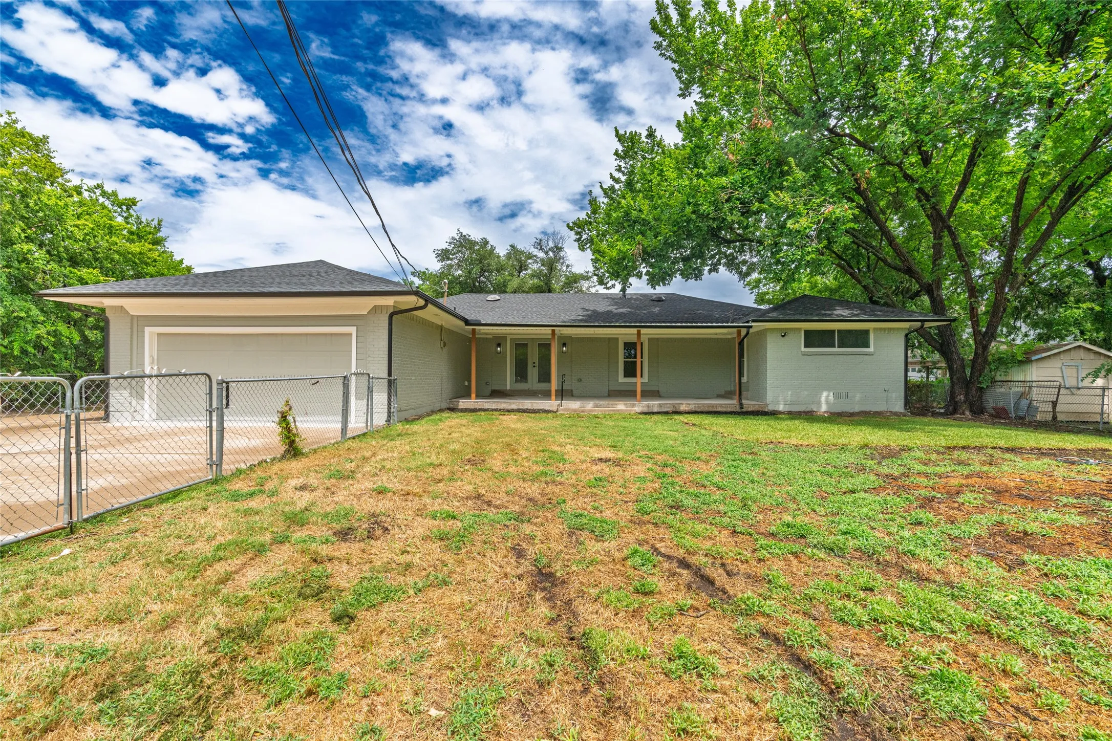 Expansive backyard featuring a covered patio, mature trees, chain-link fencing, and a detached shed