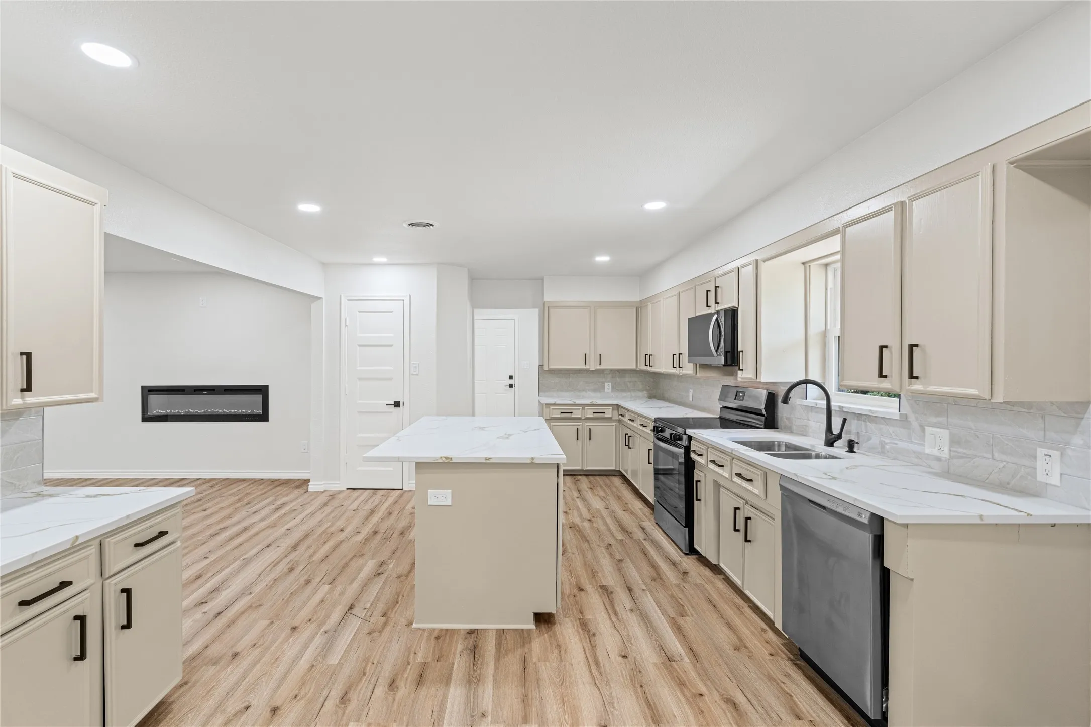Open-concept kitchen featuring light wood-finish flooring, an island with a white countertop, recessed lighting, and a linear electric fireplace