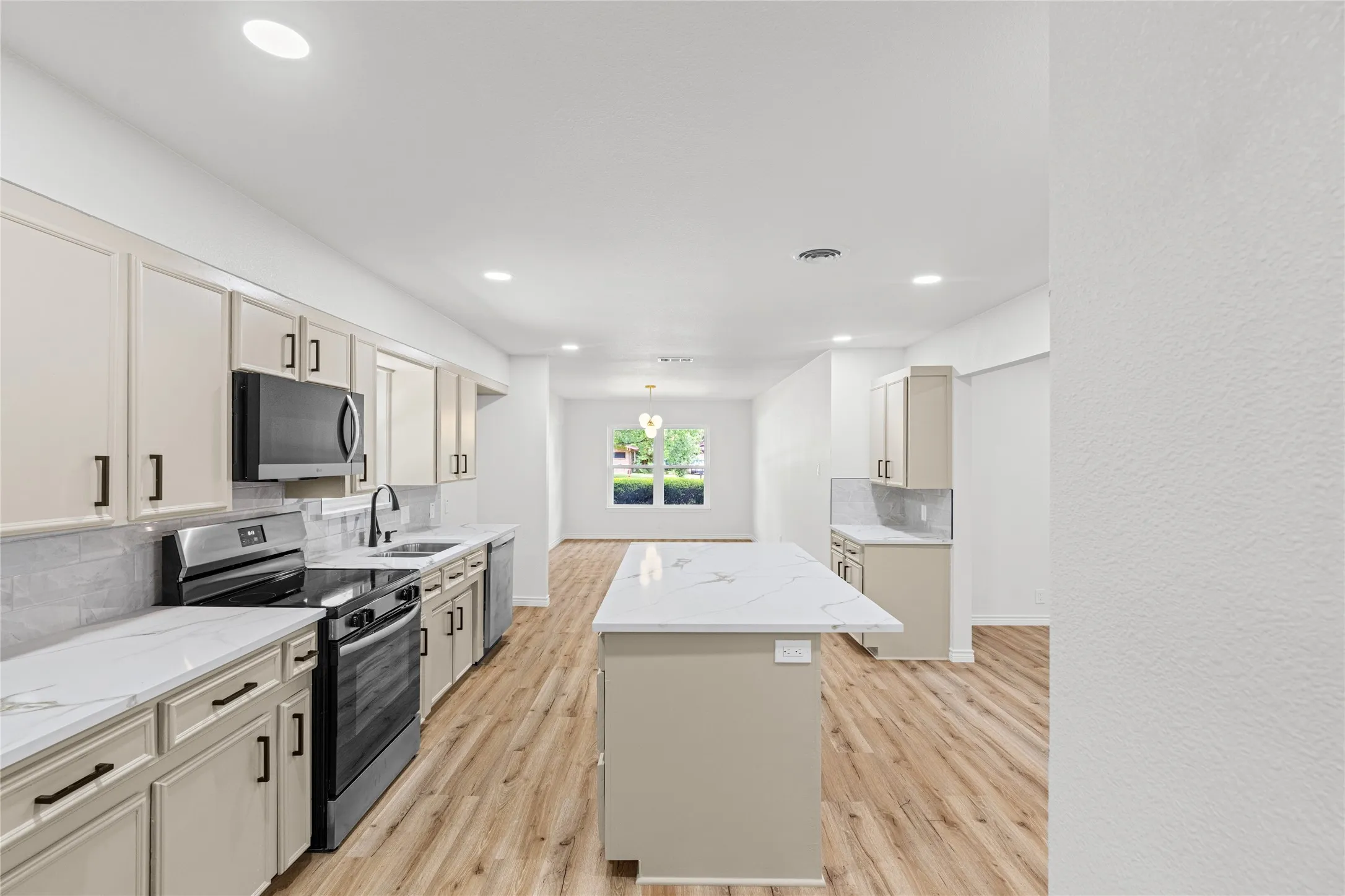 Modern kitchen featuring neutral-toned cabinetry, stainless steel appliances, a center island with a stone-finish countertop, wood-finish flooring, and recessed lighting