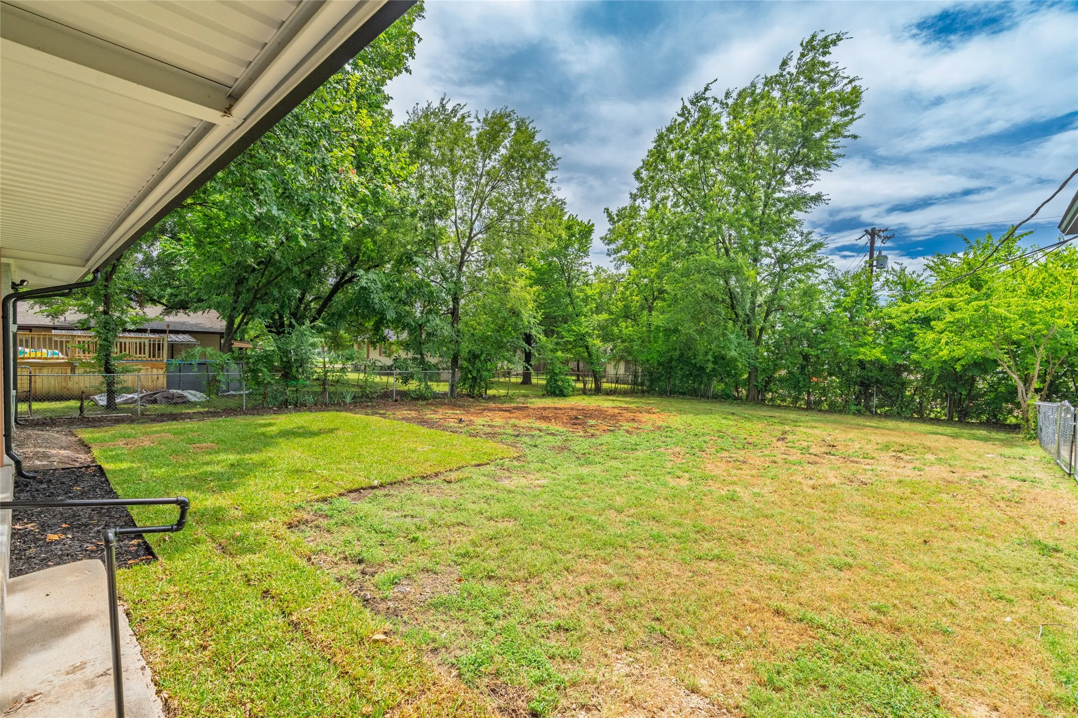 Expansive backyard featuring a large grassy area, mature trees along the perimeter, and a partial chain-link fence