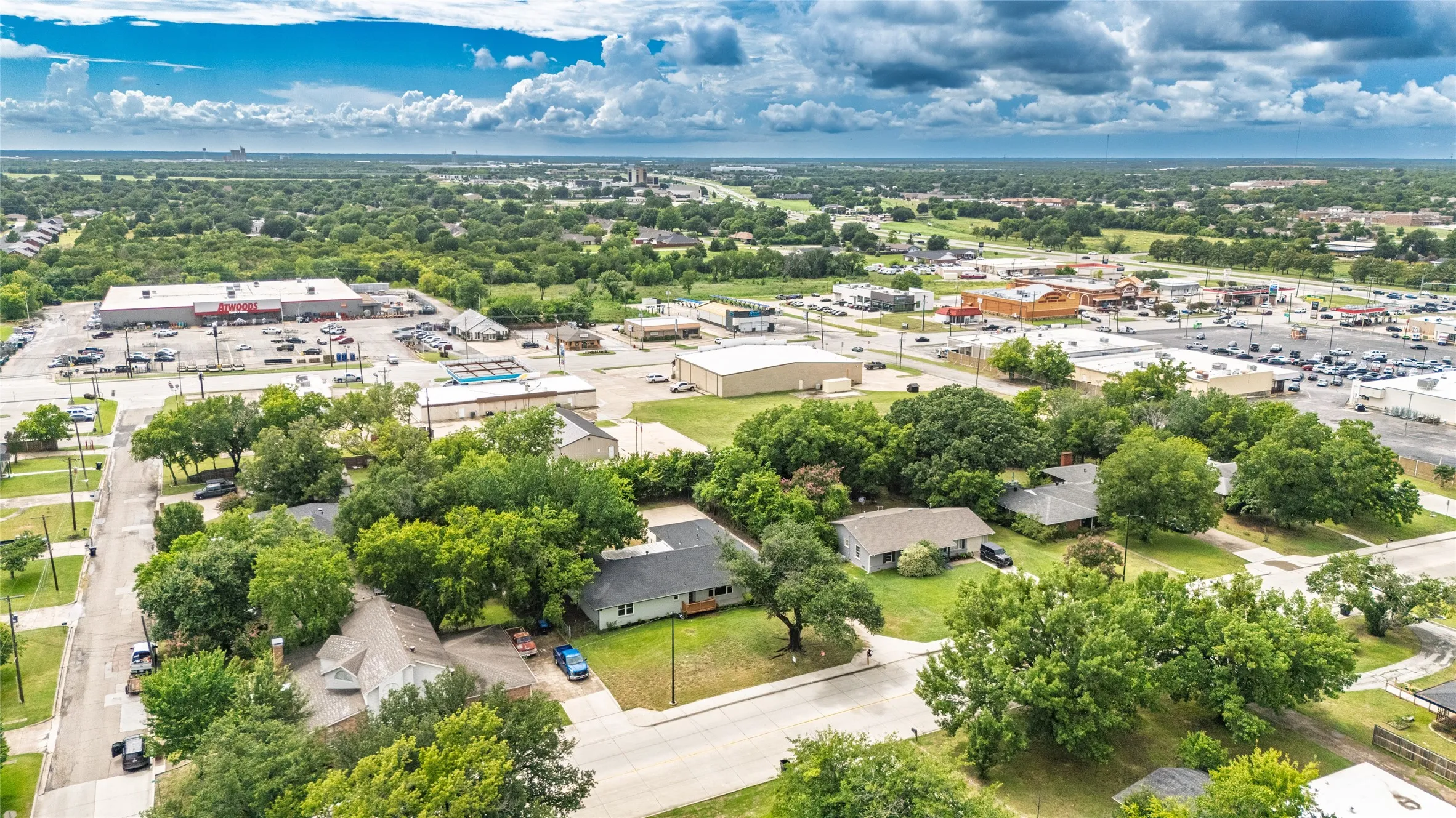 Aerial view featuring a residential neighborhood with established trees, paved streets, and a blend of single-story homes