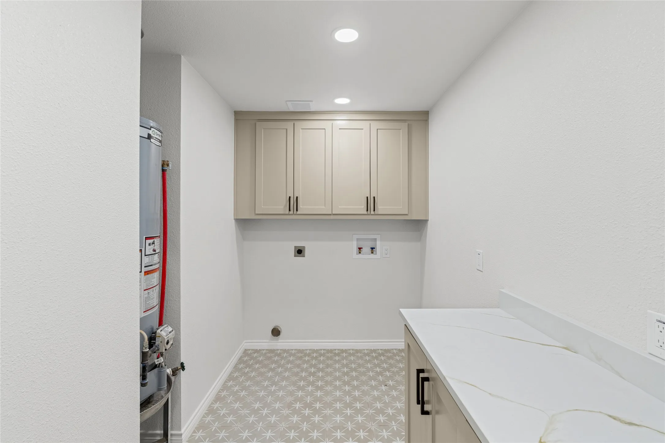 Laundry area featuring patterned floor tile, recessed lighting, upper cabinetry, an extensive countertop, and a built-in water heater