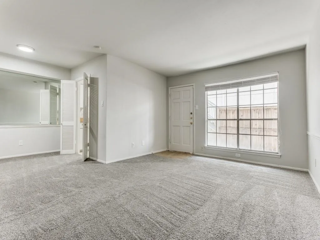 Spacious living room featuring light gray carpeting, neutral wall finishes, white trim, and a window