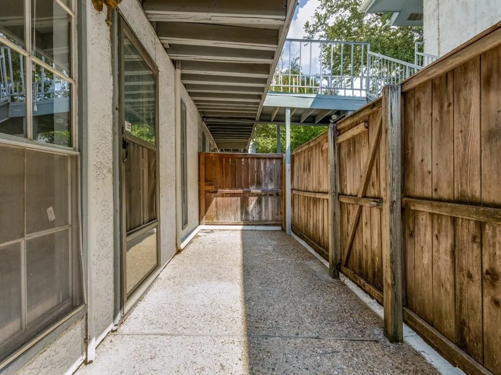 Private outdoor corridor featuring a concrete walkway, wood privacy fencing, and multiple windows