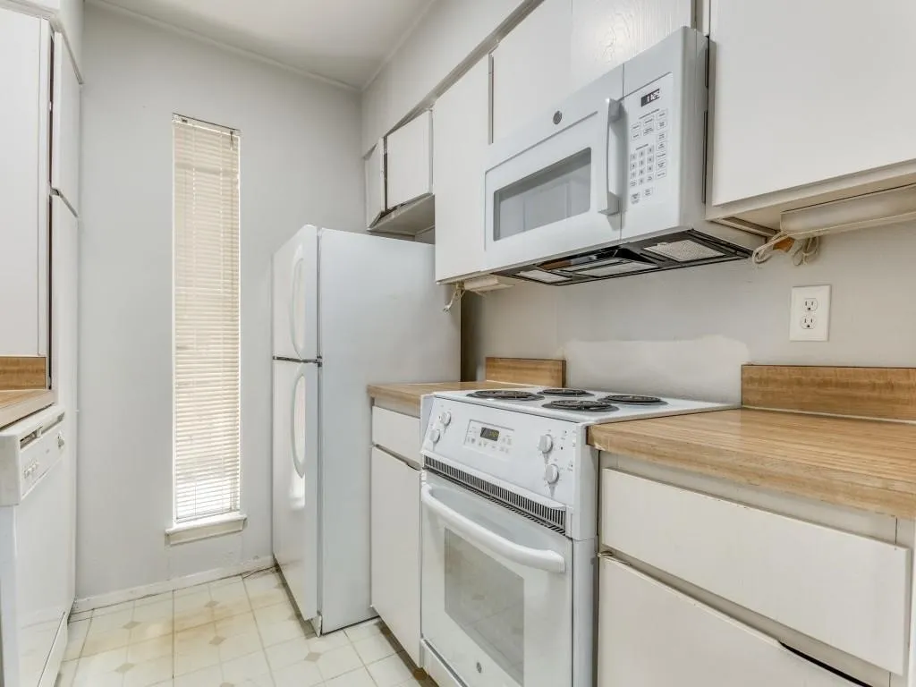 Kitchen featuring white appliances, upper and lower cabinetry, wood-finish countertops, and a vertical window with blinds