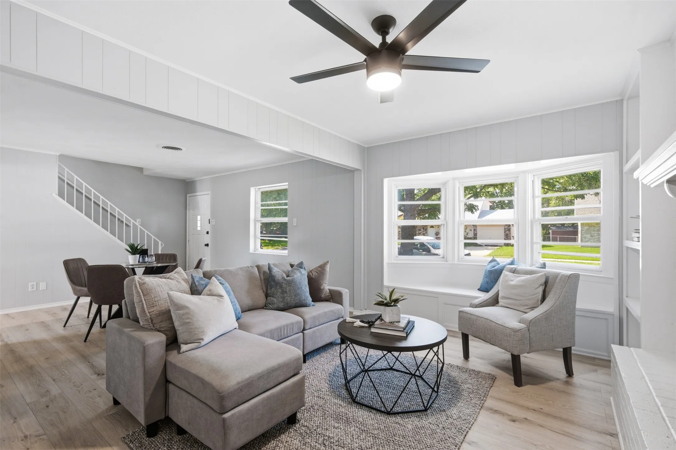 Bright Living with a Bay Window Seat — A wall of windows fills the living area with natural light, and the built-in window seat offers a cozy place to unwind while maintaining an open flow to the dining space.