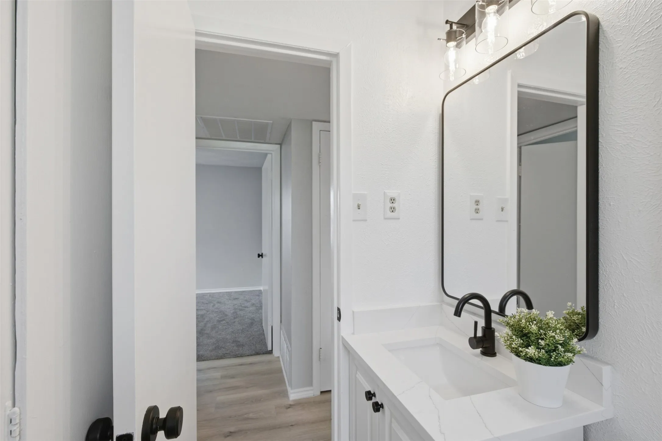 A Polished Start to the Day — The remodeled vanity area features a quartz-style countertop, undermount sink, updated lighting, and a large mirror, with convenient access from the main-level bedroom.