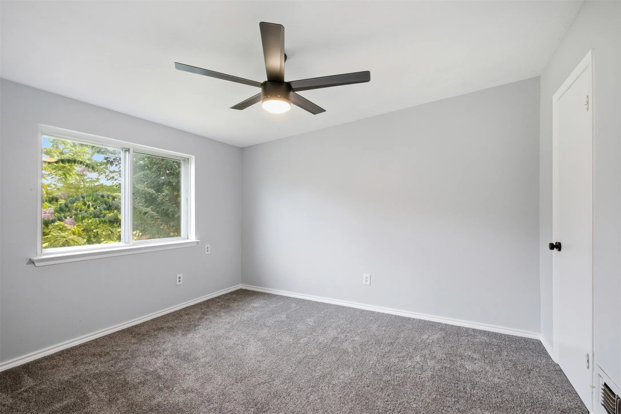 Bright Upstairs Bedroom — New carpet, fresh paint, a modern ceiling fan, and a wide window create a comfortable secondary bedroom filled with natural light.