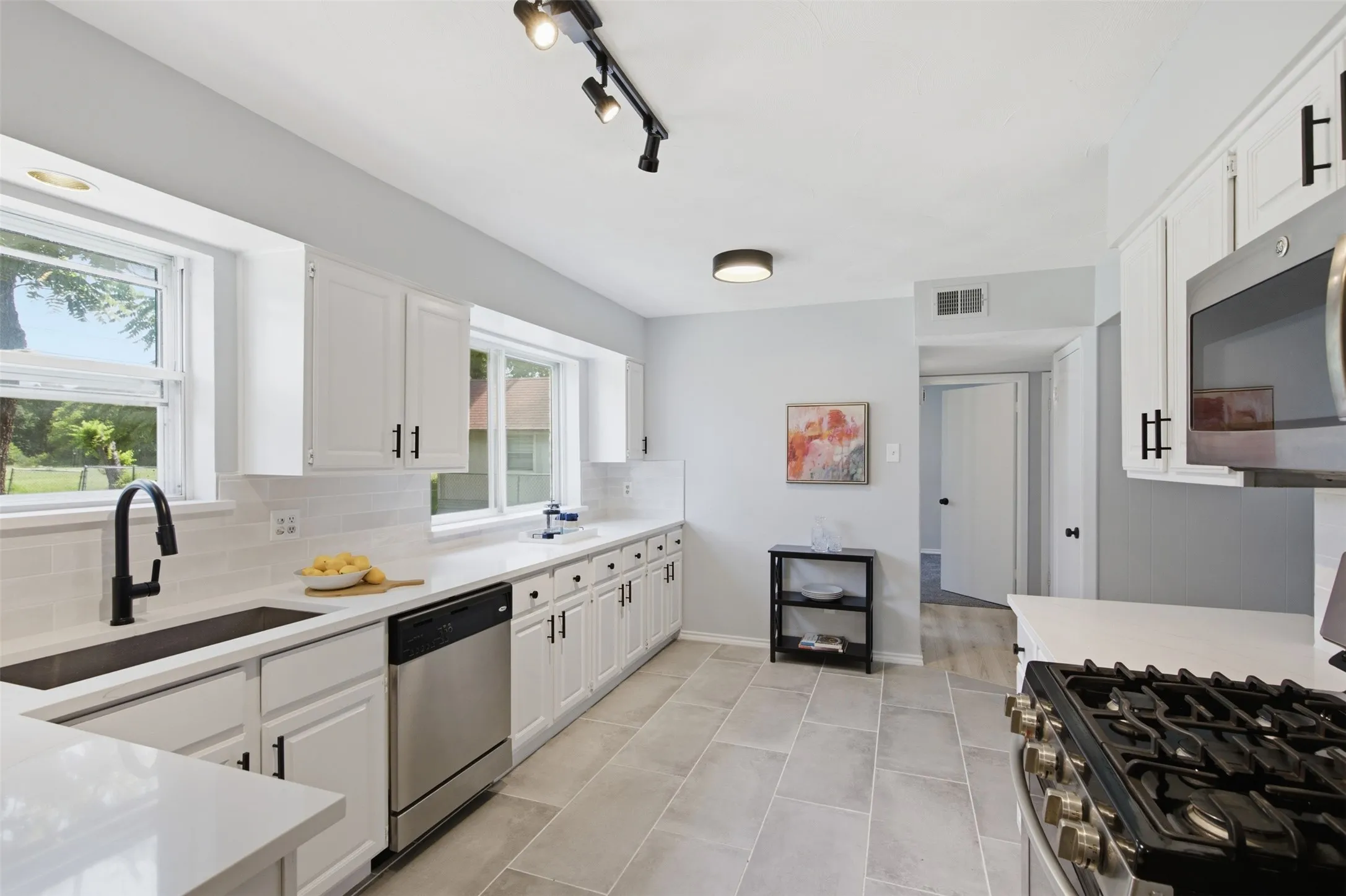 Designed for Everyday Cooking — The remodeled kitchen pairs crisp white cabinetry, generous counter space, stainless appliances, and durable tile flooring with an open connection to the dining area.