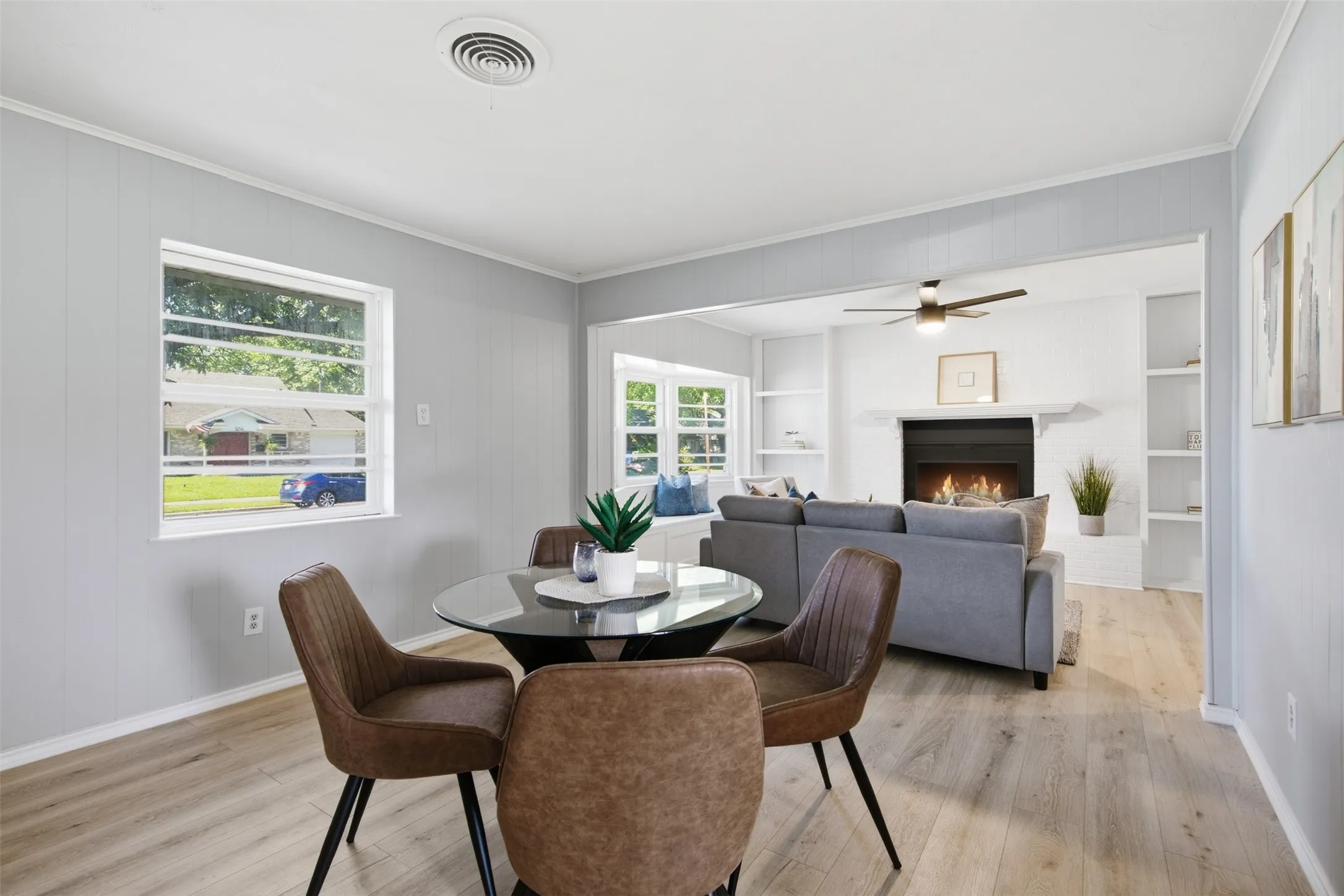 A Welcoming View Ahead — From the dining area, the brick fireplace draws the eye through a generous opening, creating a warm visual connection between the home’s main living spaces.