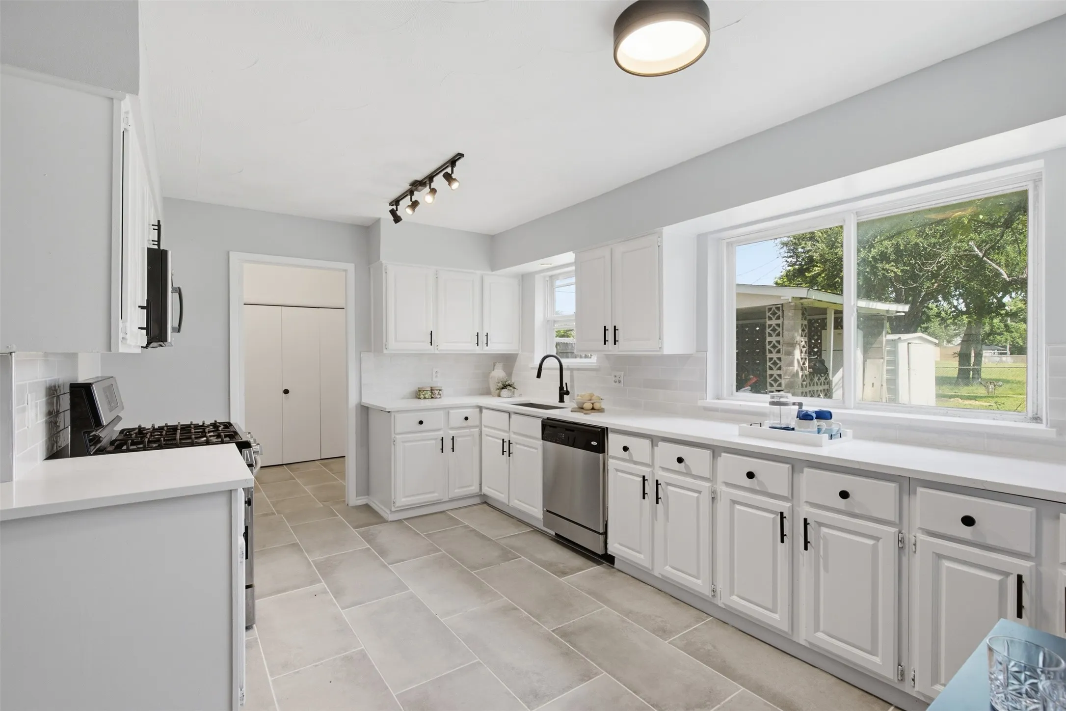 Bright, Functional Workspace — Multiple windows bring natural light across the long countertop, while abundant cabinetry, a gas range, and an efficient work triangle make meal preparation feel effortless.
