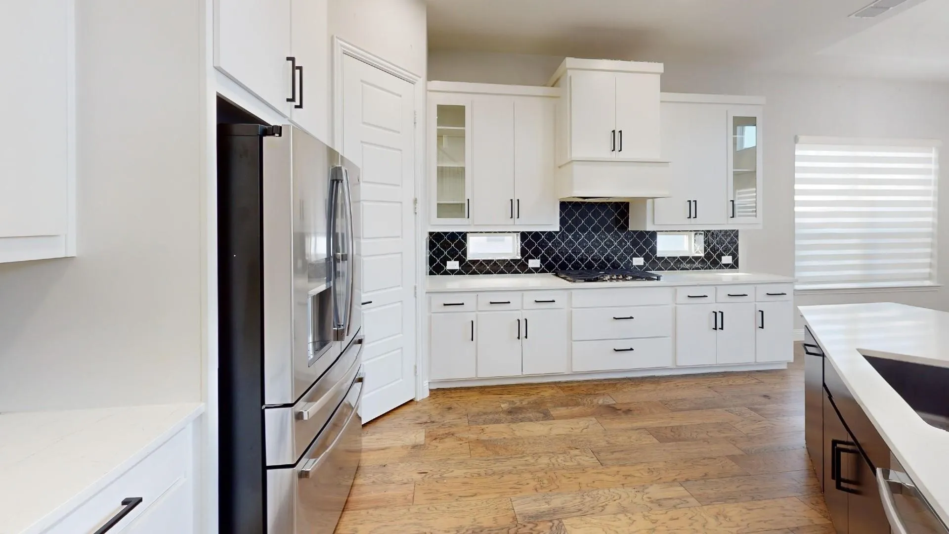 Modern kitchen featuring white cabinetry, a dark patterned tile backsplash, stainless steel appliances, and wood-finish flooring