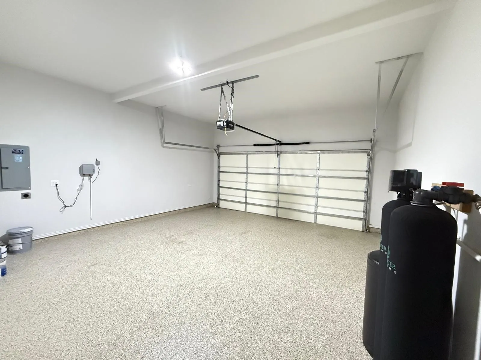 Spacious garage featuring a durable epoxy floor coating, automatic garage door opener, overhead lighting, and white painted walls
