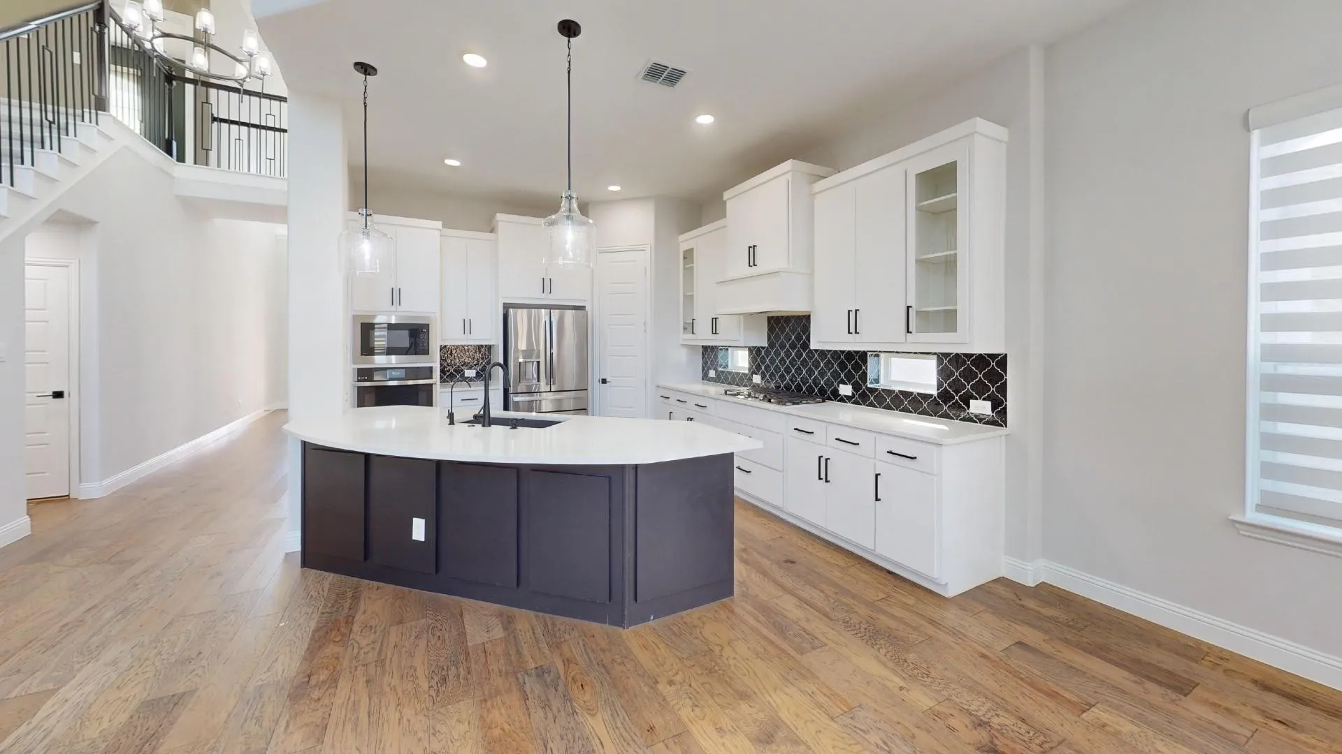Expansive kitchen featuring a curved island with dark cabinetry, white countertops, and pendant lighting