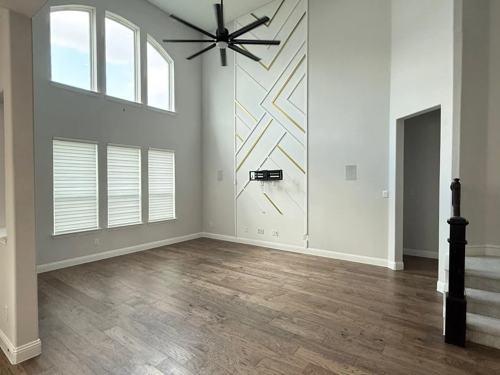 Spacious room featuring high ceilings, wood-finish flooring, and a contemporary accent wall with geometric detailing