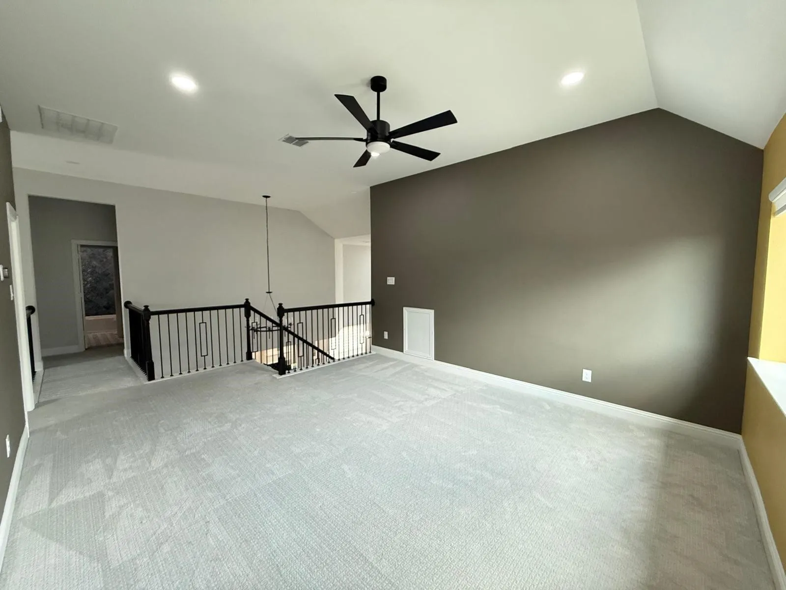 Spacious loft area featuring vaulted ceilings, a contemporary ceiling fan, recessed lighting, soft gray carpeting, and black wrought iron balusters