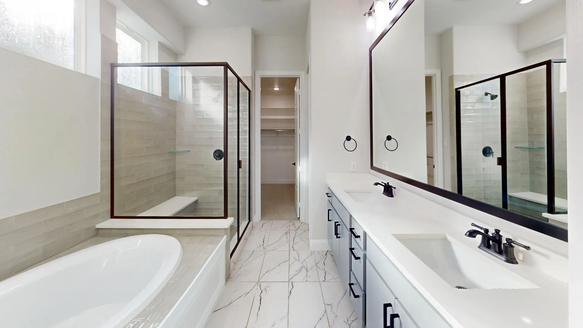 Spa-inspired bathroom featuring a freestanding tub, glass-enclosed shower with bench seating, dual vanity with solid surface countertop, matte black fixtures, and patterned tile flooring