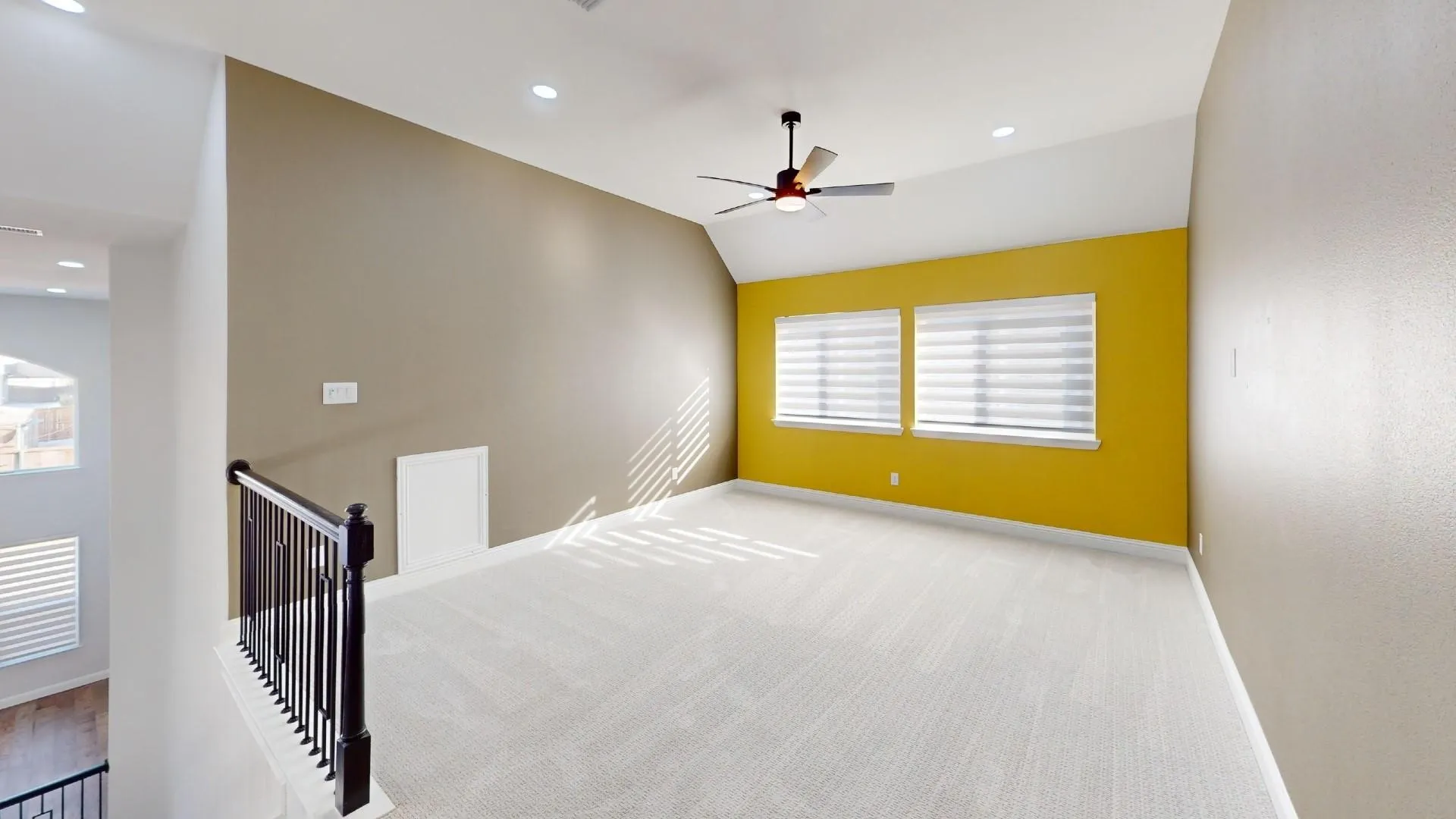 Spacious loft area featuring light-toned carpeting, two windows with blinds, a ceiling fan, and recessed lighting