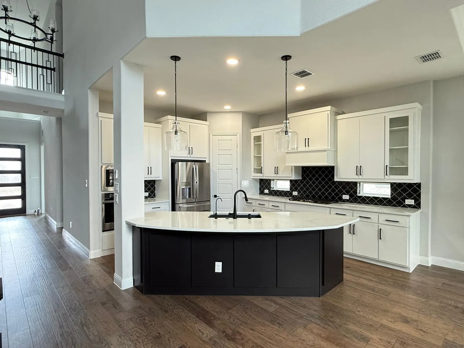 Modern kitchen featuring a curved island with dark cabinetry, light countertops, and clear pendant lighting