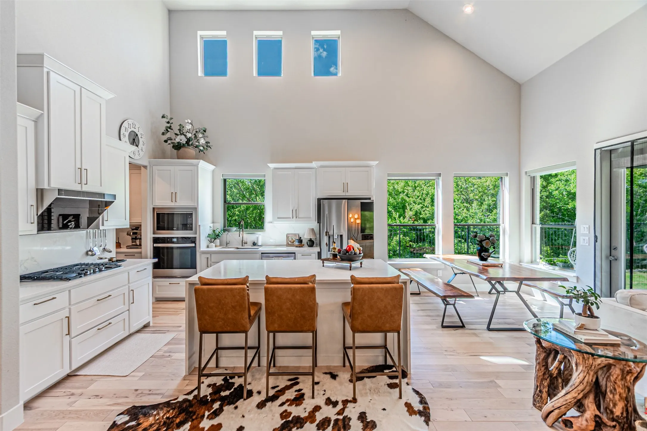 Open-concept kitchen and dining area featuring a vaulted ceiling, light wood-finish flooring, white cabinetry, a kitchen island with seating, and a built-in oven and microwave