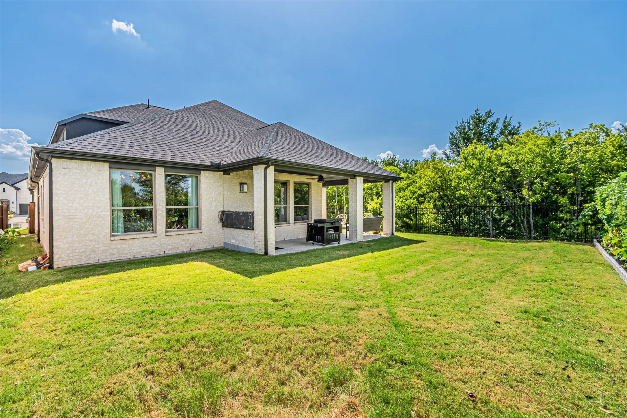 Spacious backyard featuring a covered patio, extensive lawn area, mature perimeter trees, light brick exterior, and dark shingle roofing