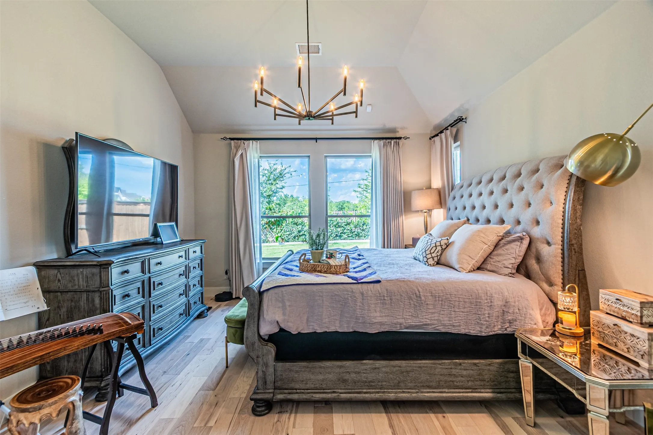 Vaulted ceiling bedroom featuring wood-finish flooring, a contemporary chandelier, and French doors with exterior views
