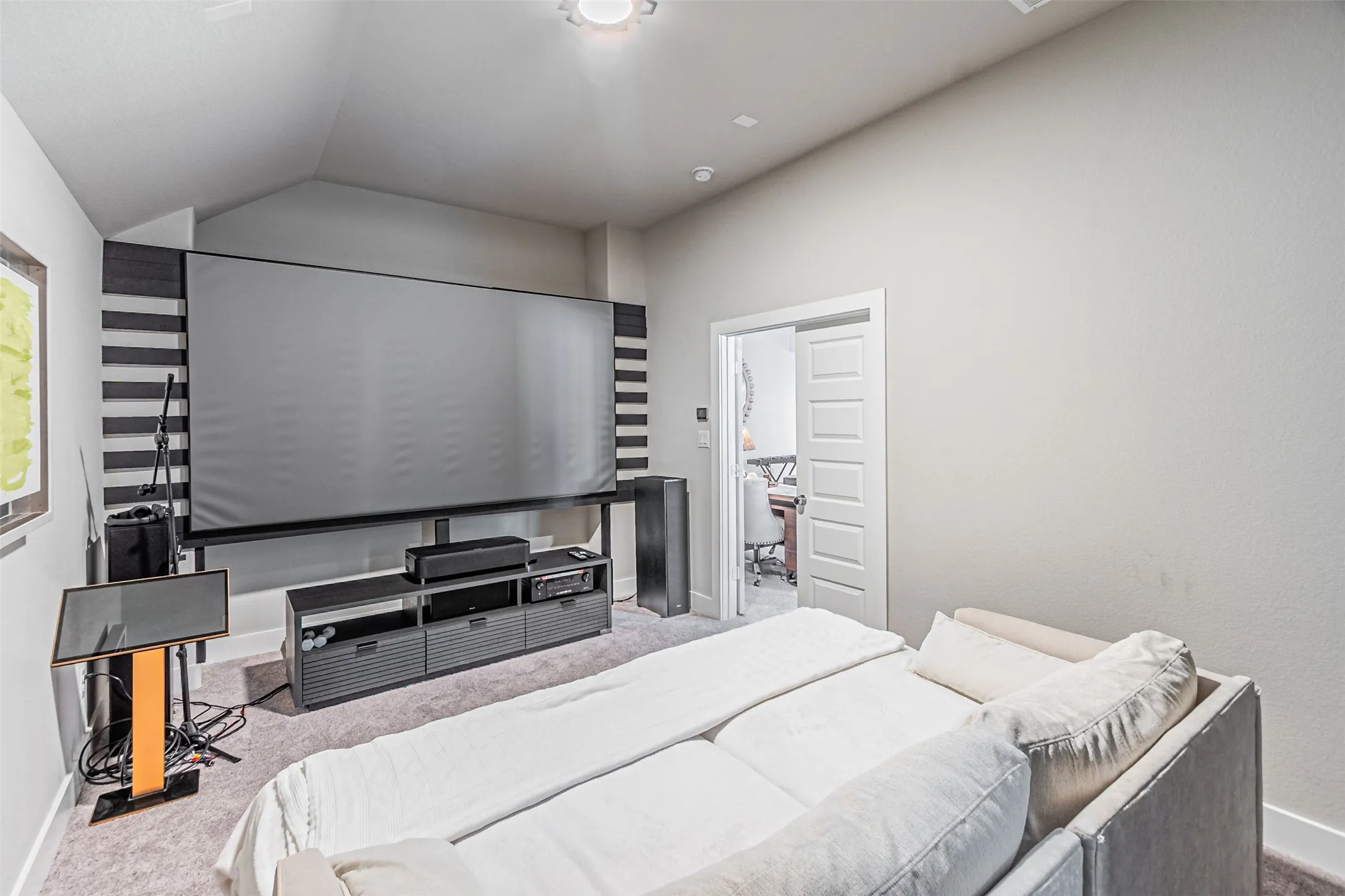 Dedicated media room featuring a large projection screen, vaulted ceiling, built-in entertainment console, light gray carpeting, and recessed lighting