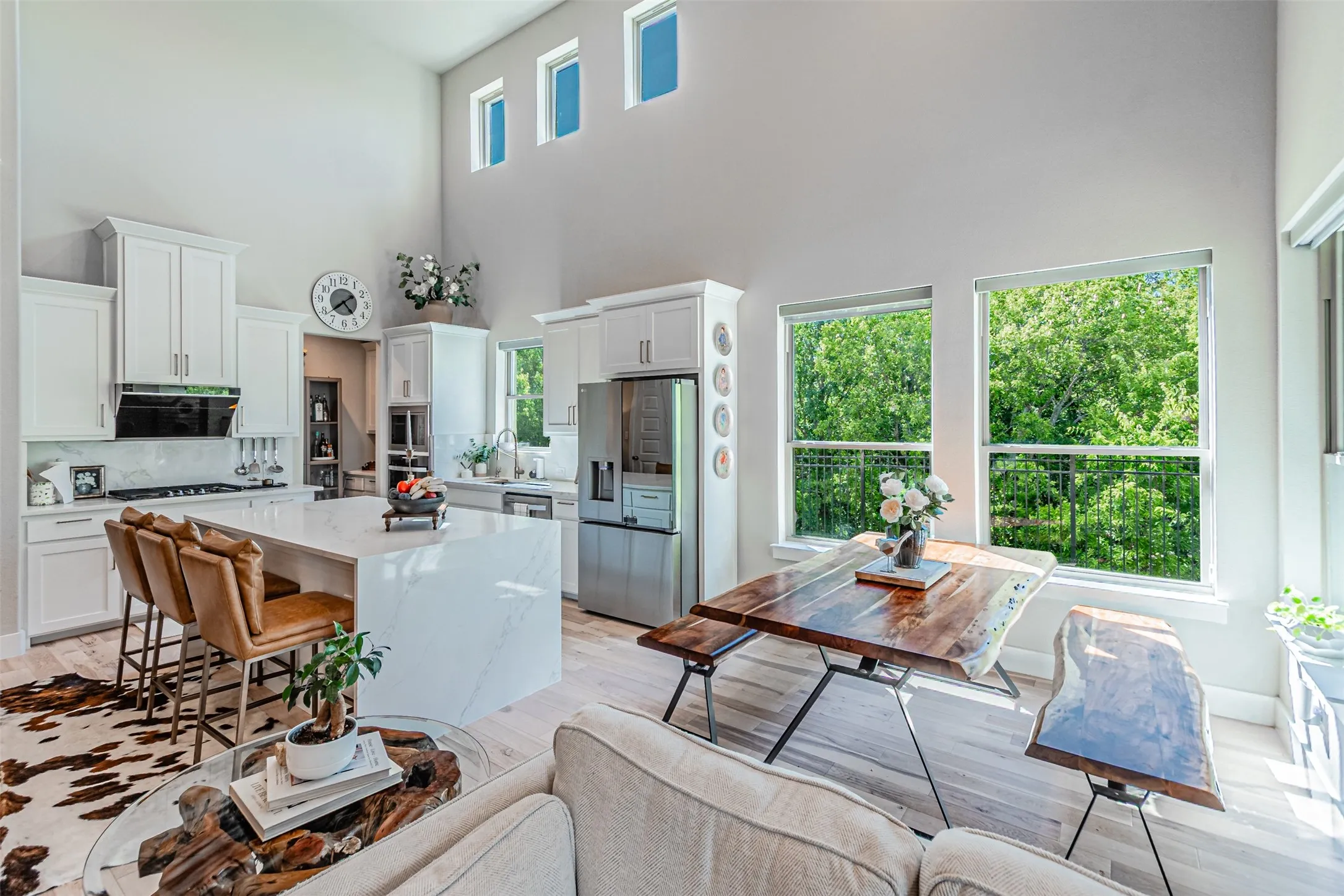 Vaulted ceilings amplify this open-concept space featuring a gourmet kitchen with white shaker cabinetry, a waterfall island with stone countertops, and stainless steel appliances