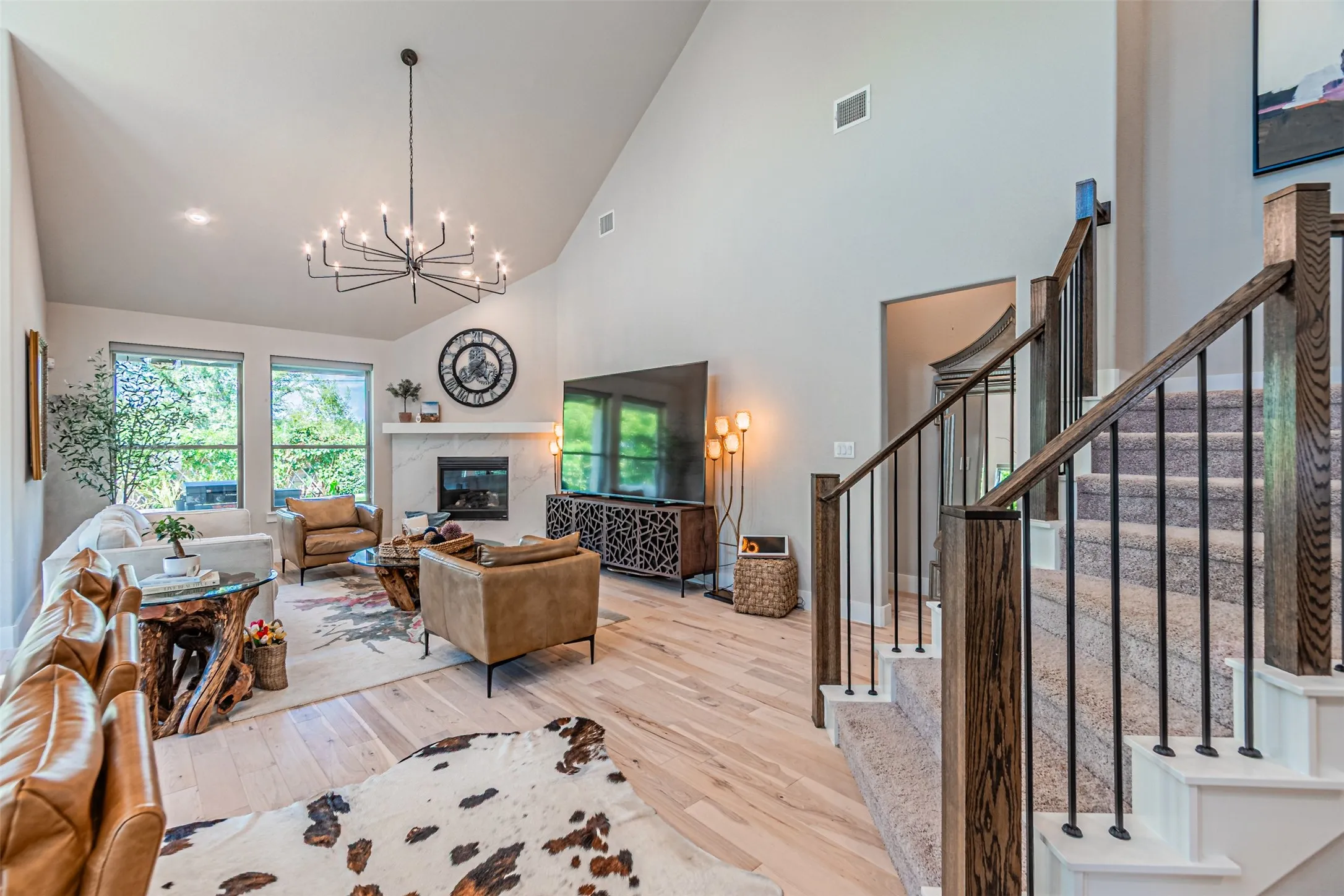 Vaulted living area featuring light wood-finish flooring, a fireplace with a stone surround, and an elegant chandelier