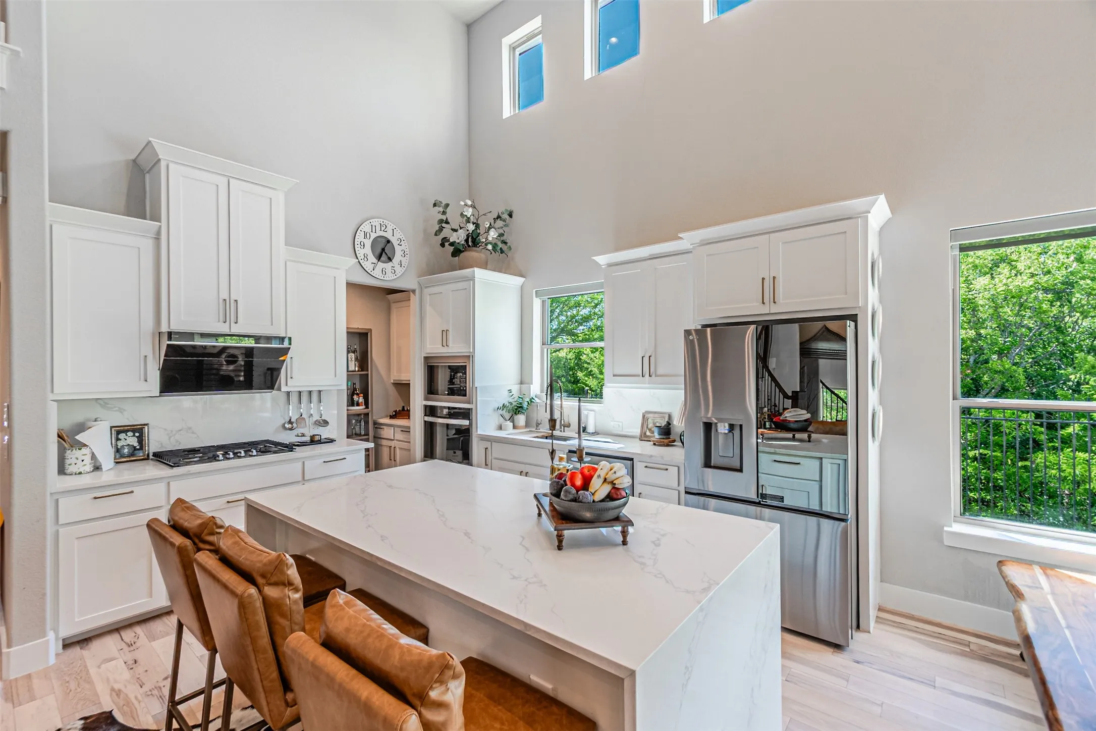 Spacious kitchen featuring a large waterfall-edge island with seating, white shaker cabinetry, stainless steel appliances, and wood-finish flooring