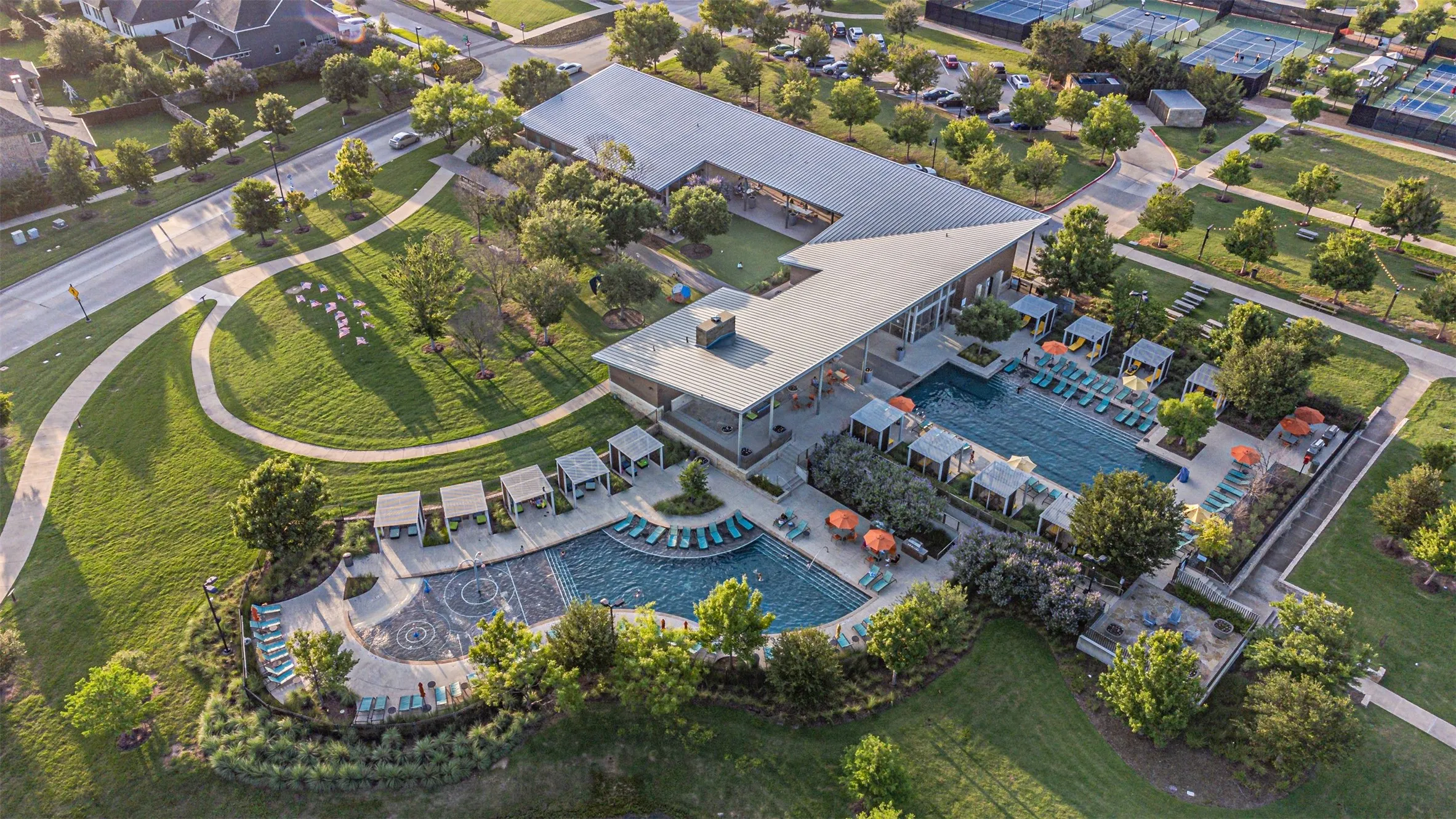 Expansive community amenity center featuring a contemporary architectural style, multiple outdoor pools, private cabanas, and extensive green spaces with walking paths