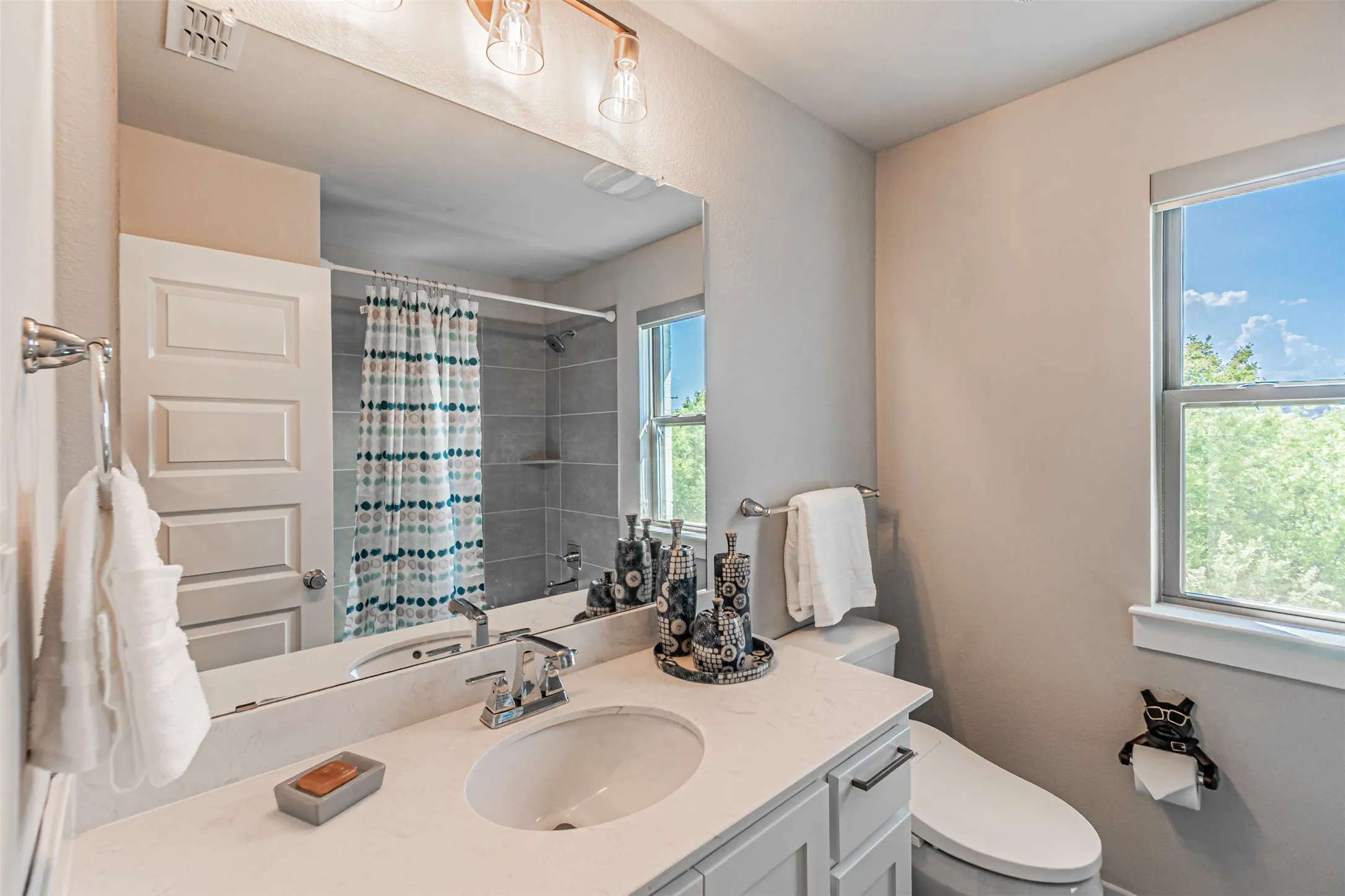 Bathroom featuring a vanity with an integrated sink and light-toned countertop, a large mirror, and a window providing natural illumination