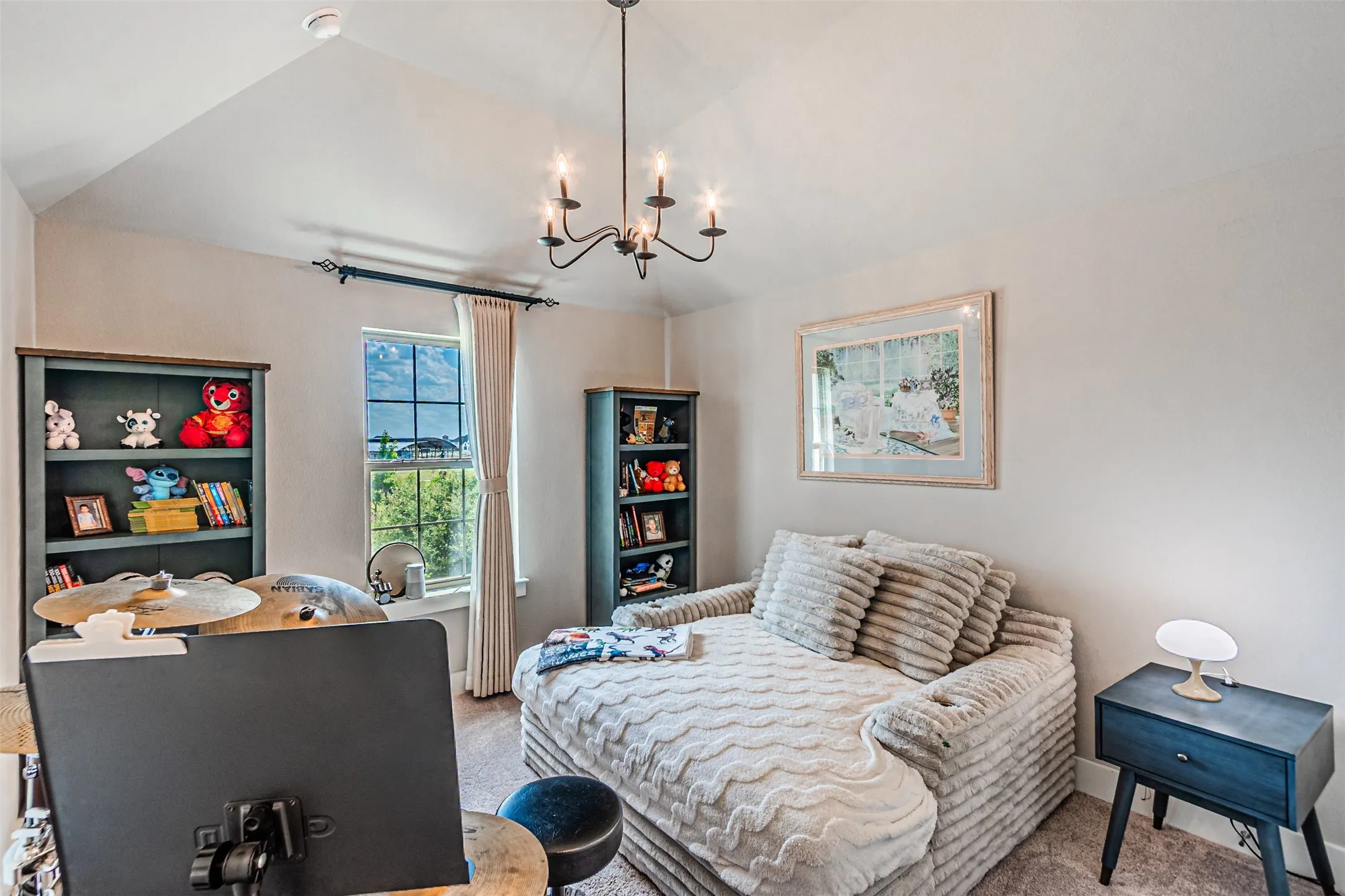 Vaulted ceiling featuring a black iron chandelier, a window with exterior landscape, and two built-in bookcases