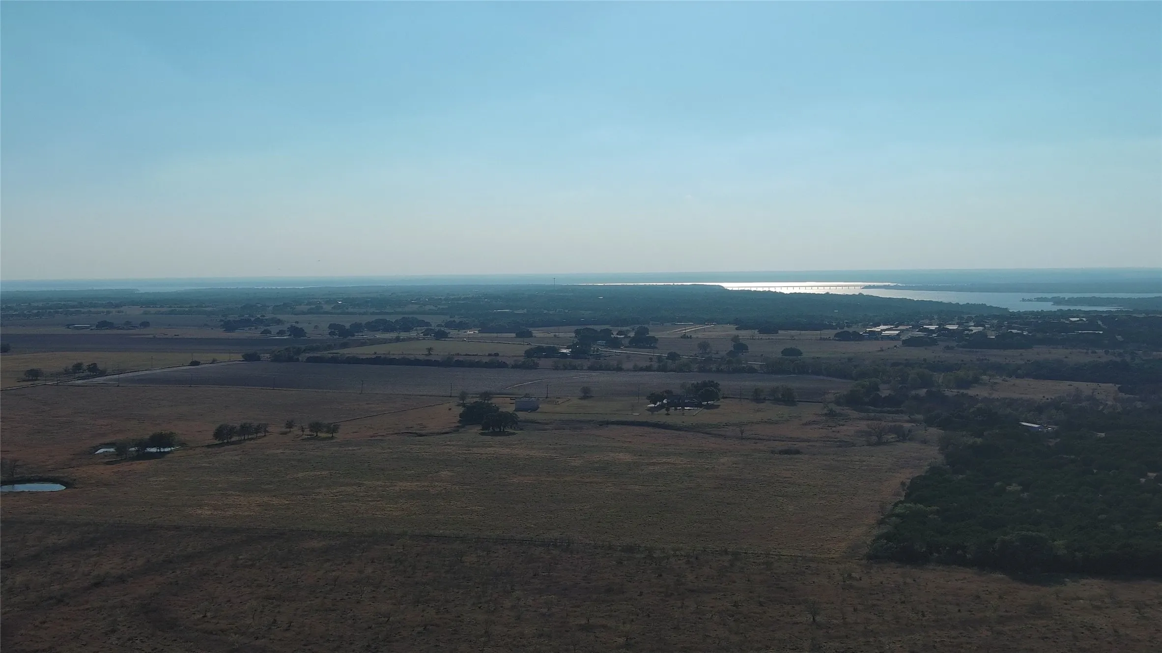 Expansive rural landscape featuring a large body of water in the distance, varied topography, and scattered trees