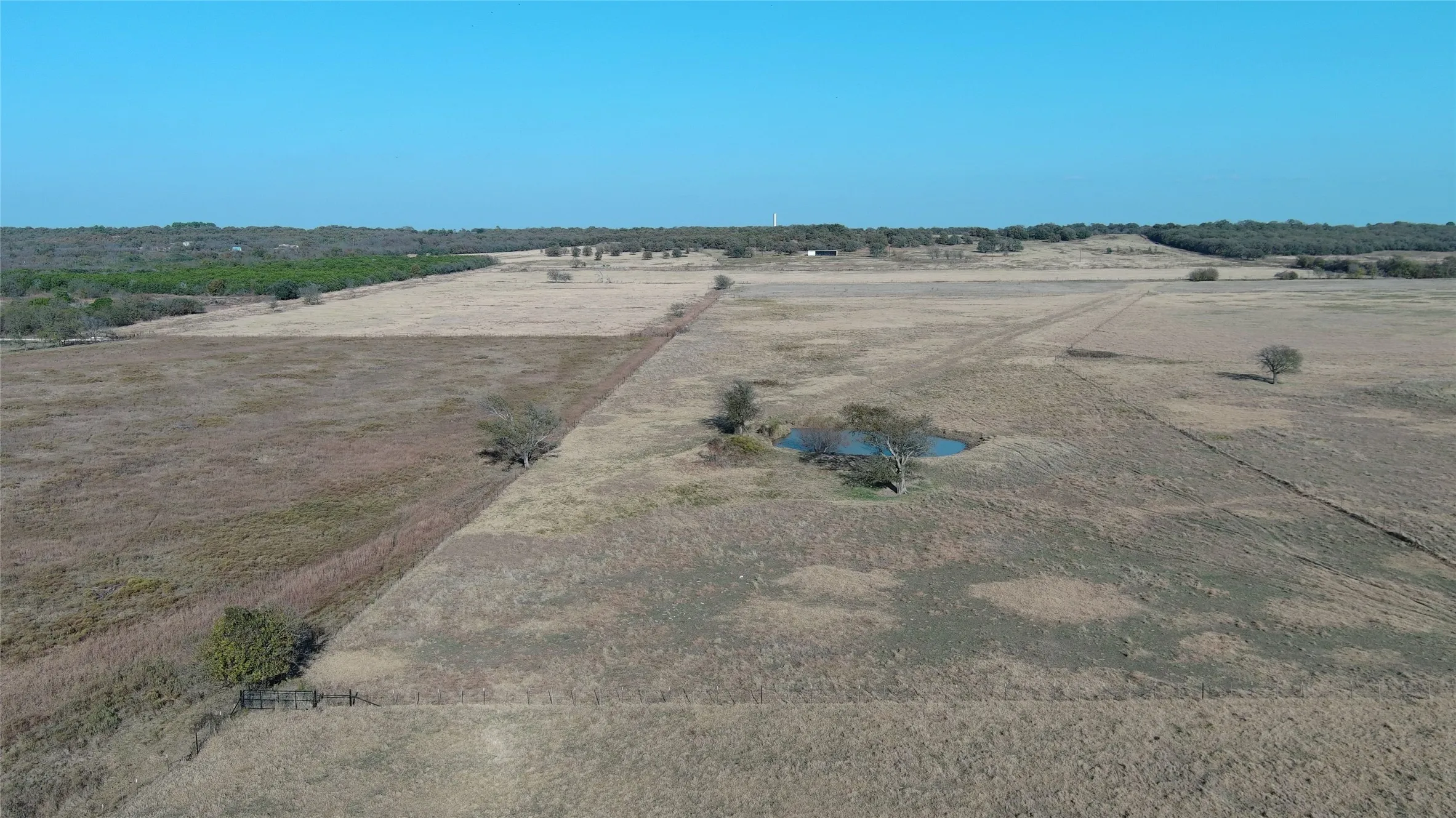 Expansive open acreage featuring a natural water feature, scattered mature trees, and a clear blue sky